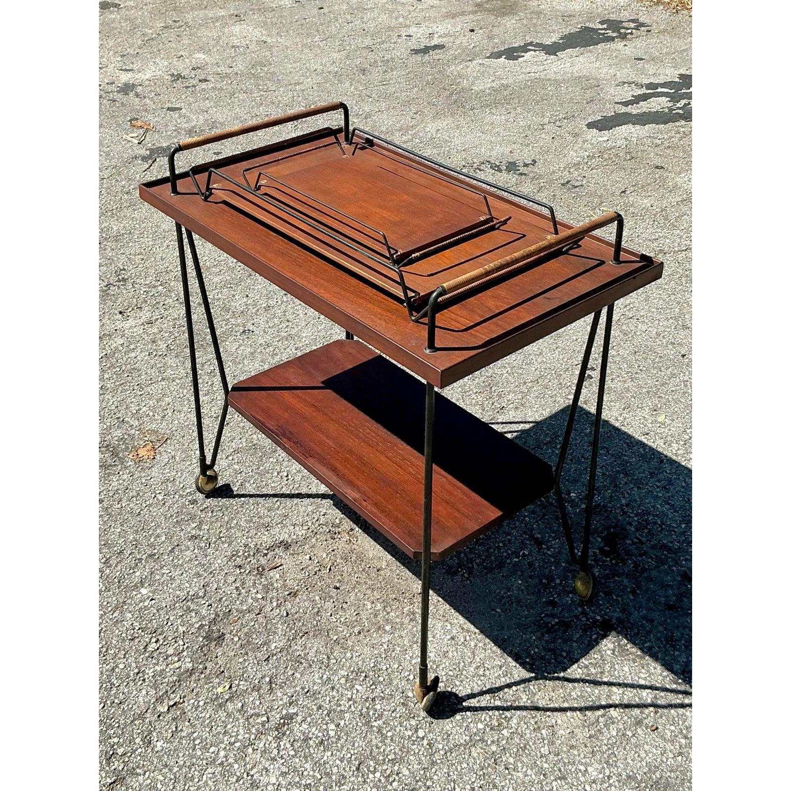This stunning Mid-Century Modern Swedish teak bar cart is a sophisticated blend of function and timeless Scandinavian design. Featuring a sleek wood grain surface, minimalist black metal frame, and warm teak tones, this piece is both stylish and