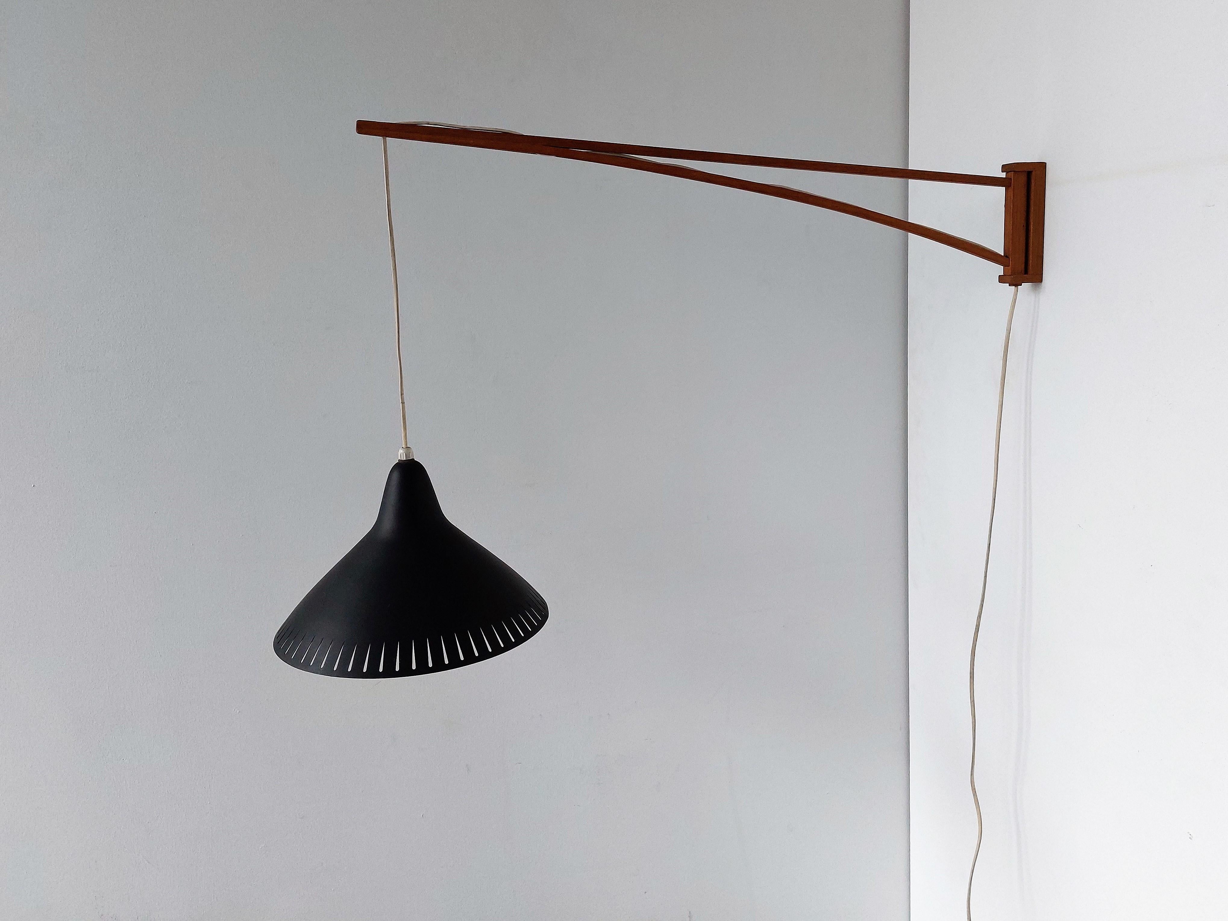 A beautiful wall lamp from the 1950's. It has an elegant wooden swing arm that holds a nicely shaped black metal shade with perforated details. This design is most likely of or inspired by the designs of the Finnish designer Lisa Johansson-Pape (for