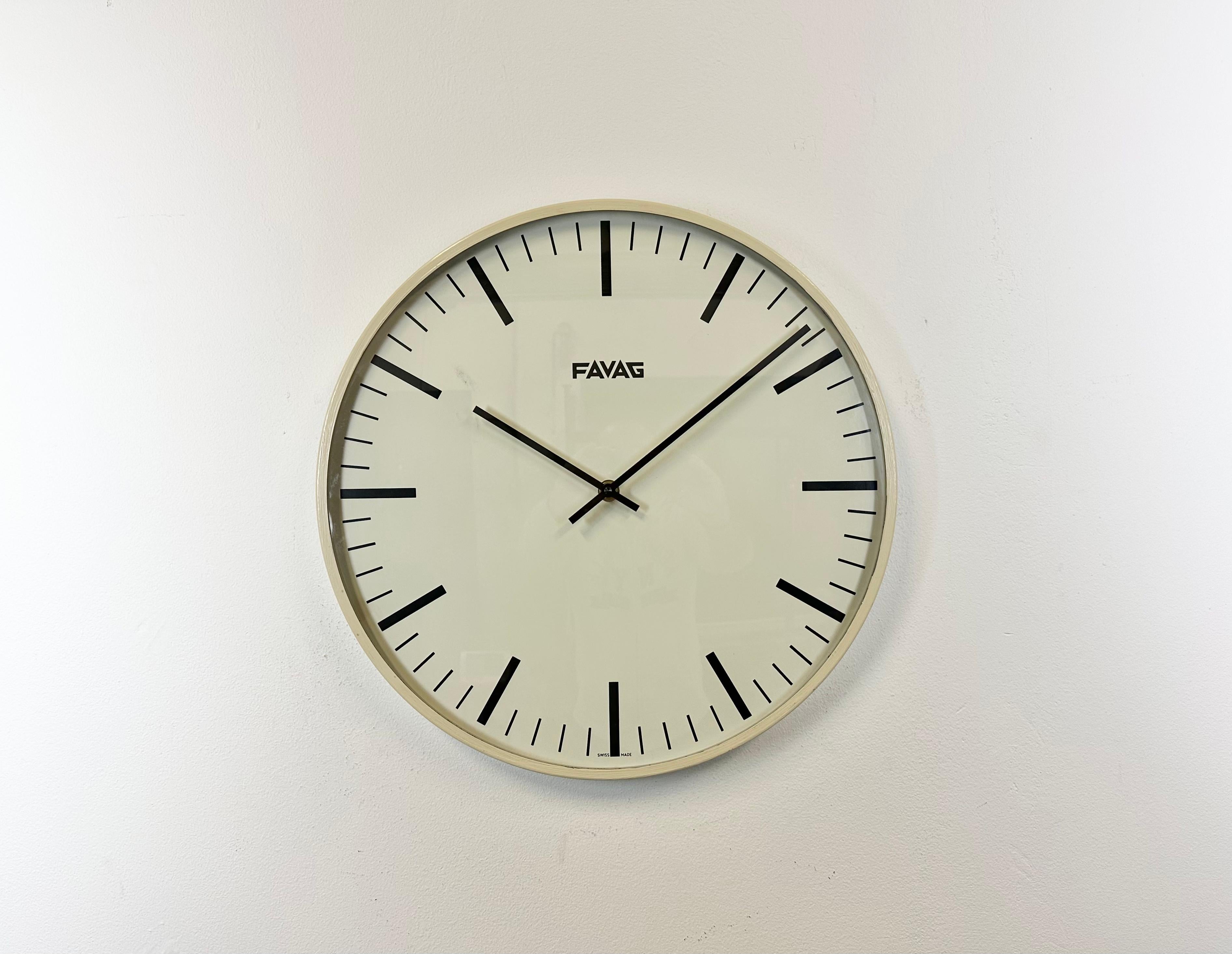 Industrielle Wanduhr, hergestellt von Favag in der Schweiz in den 1970er Jahren. Sie hat einen beigen Eisenrahmen, ein Aluminiumzifferblatt und -zeiger sowie eine gewölbte Klarglasabdeckung. Das Stück wurde in ein batteriebetriebenes Uhrwerk