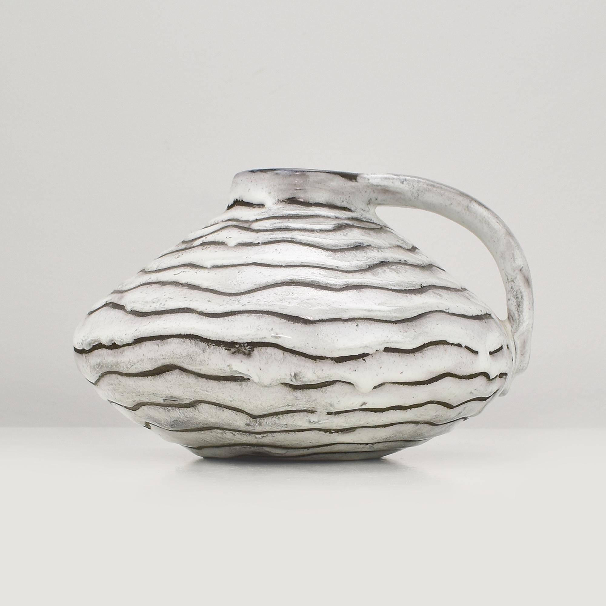 Un vaso da fiori piatto con un ampio manico applicato e uno spesso smalto bianco a onde su sfondo nero opaco, disegnato da Gustav Spörri per il produttore Ziegler Schaffhausen negli anni Cinquanta. Questo pezzo sorprendente combina contrasti audaci