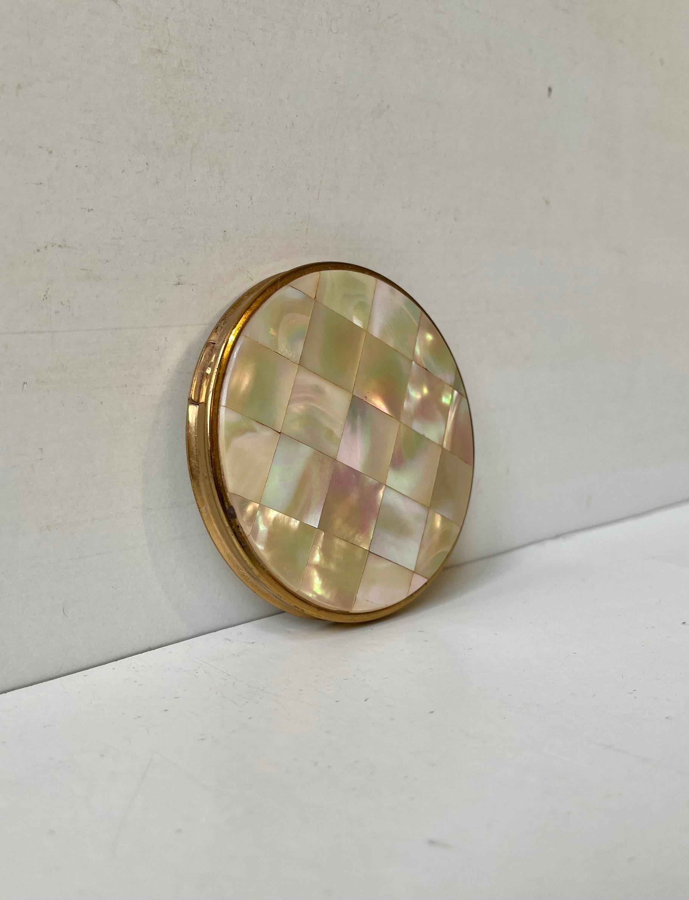 A stylish vintage powder compact with mirror executed in gold plated metal and showcasing a front tiled with mother of pearl. Swiss made circa 1930-60. Measurements: D: 8 cm, H:dept: 1.4 cm.