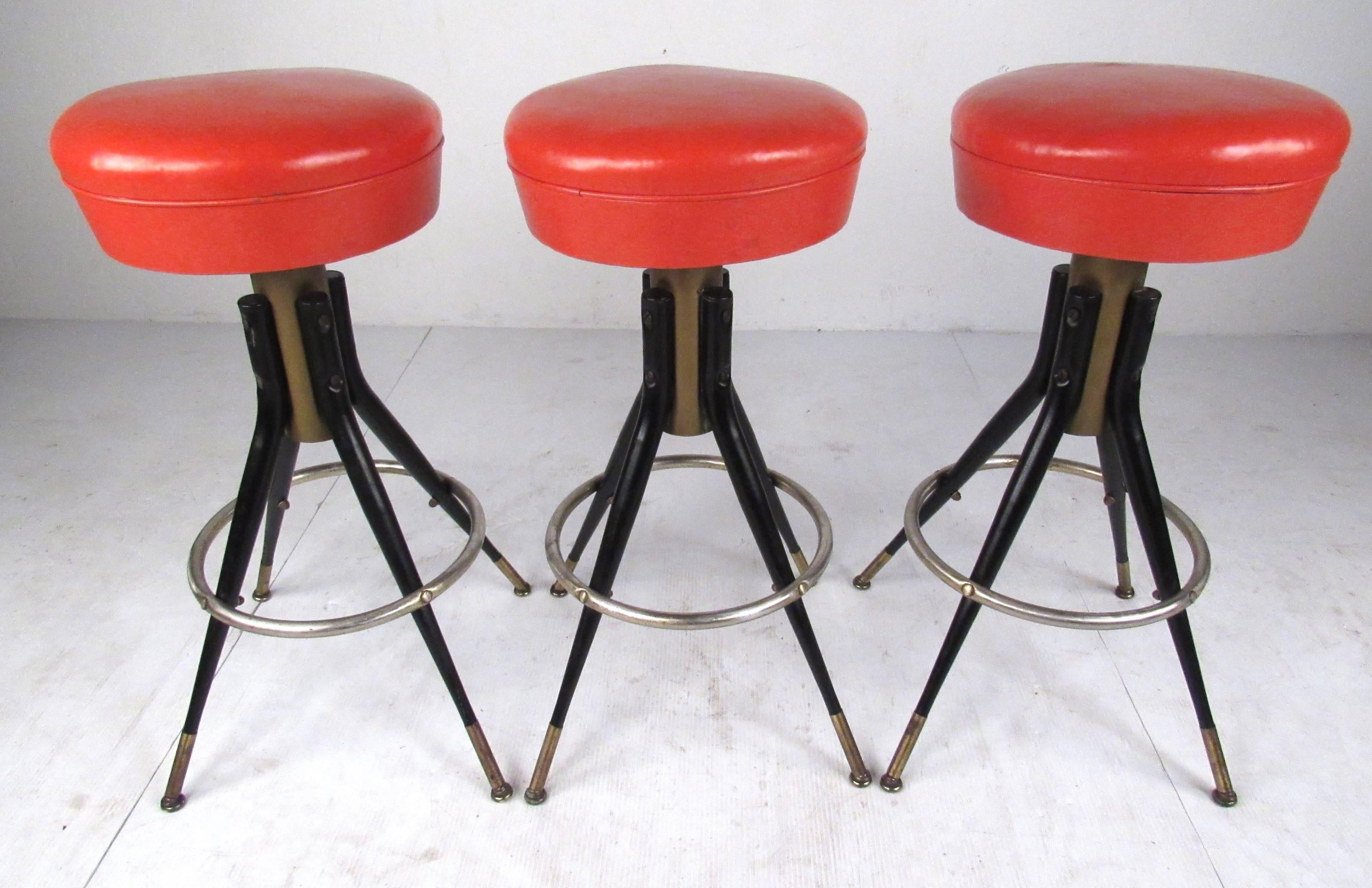 Set of three swivel stools with bright orange vinyl seats from the L & B Products Corp., Brooklyn, NY. Very well constructed with metal base and legs, footrest, and brass sabots. Nice retro look with a combination of industrial and midcentury
