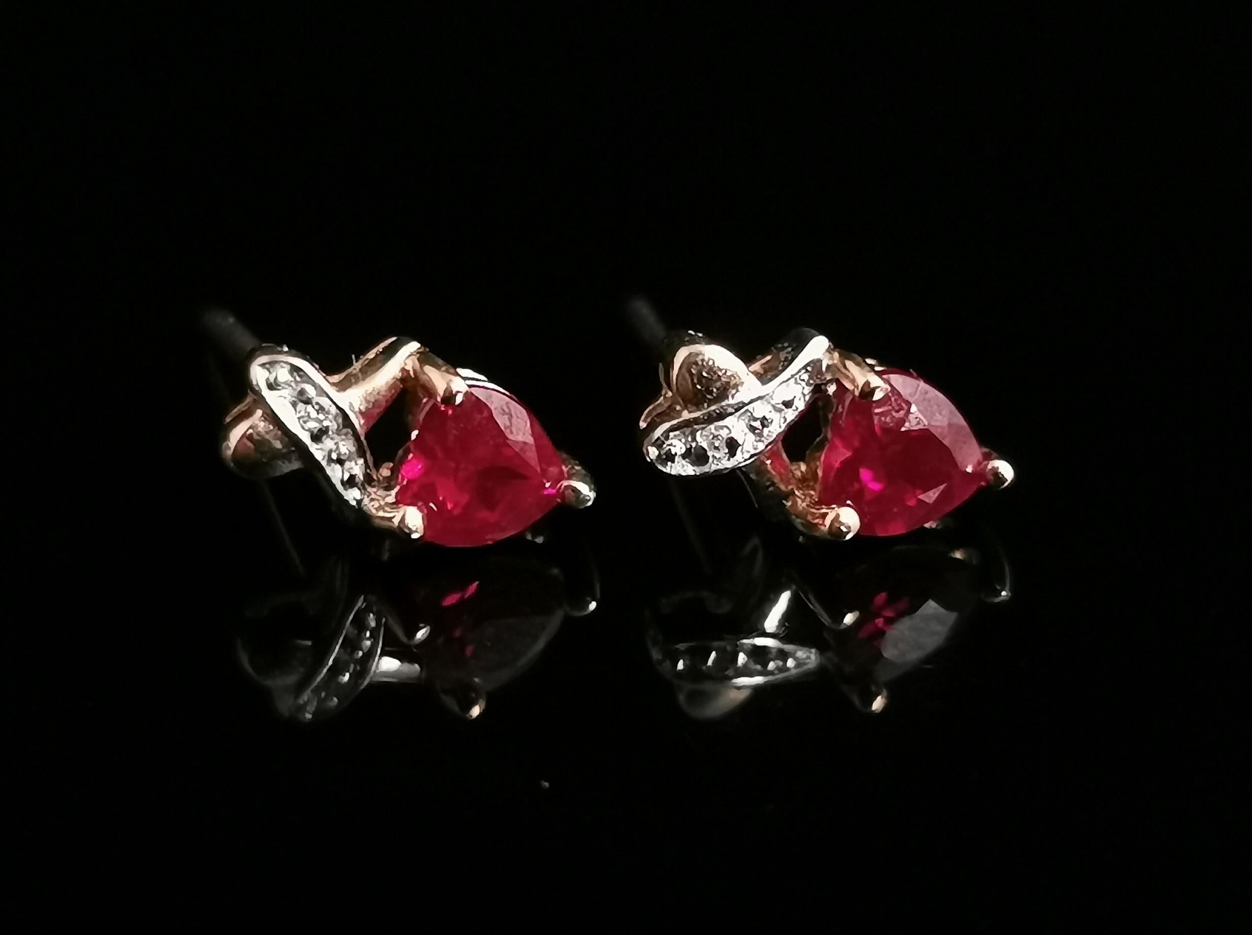 A pretty pair of vintage Synthetic Ruby and Diamond heart shaped stud earrings in 9kt yellow and white gold.

The rubies have a deep red pink hue and are cut in a heart shape, above each Ruby is a scroll of white gold set with tiny diamond