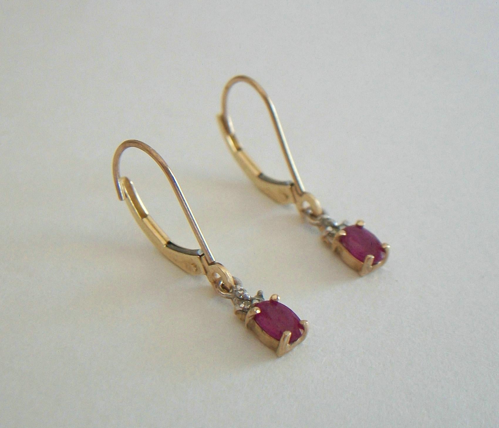 Vintage delicate pair of 10K yellow gold pendant earrings - each earring featuring a synthetic Ruby (prong set - oval faceted cut - 6.0 x 3.5 x 2.5 mm. - approx. .35 carats each) - above each ruby are 3 small diamonds set in white gold (claw set -