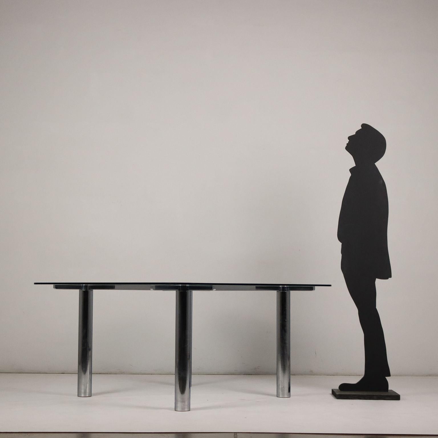Tavolo con base in metallo cromato e piano in vetro.