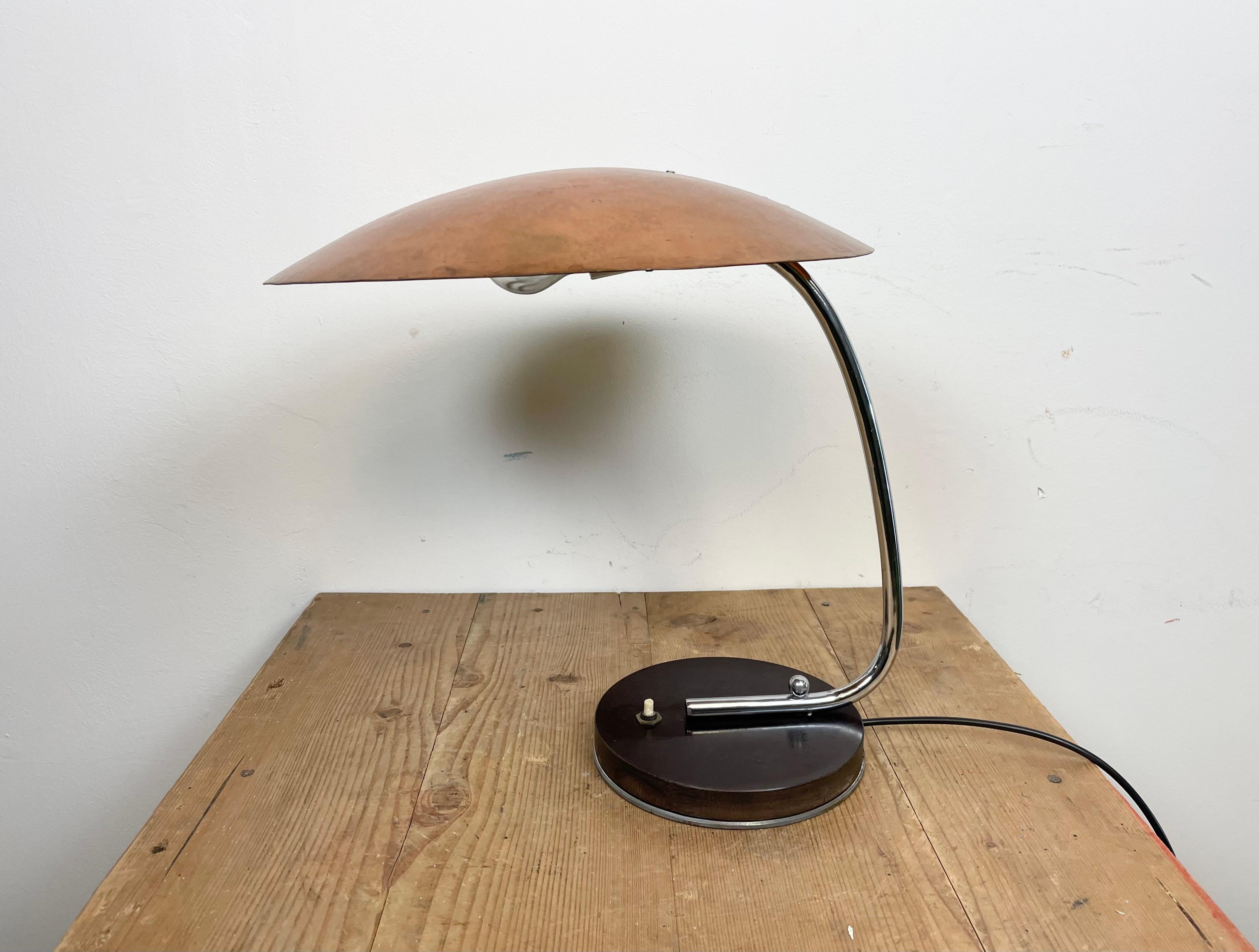 This vintage table lamp was produced in former Czechoslovakia during the 1970s. It features a brass lampshade, a chrome plated arm and a bakelite base with switch. The original socket requires standard E 27/ E 26 light bulbs. Good vintage