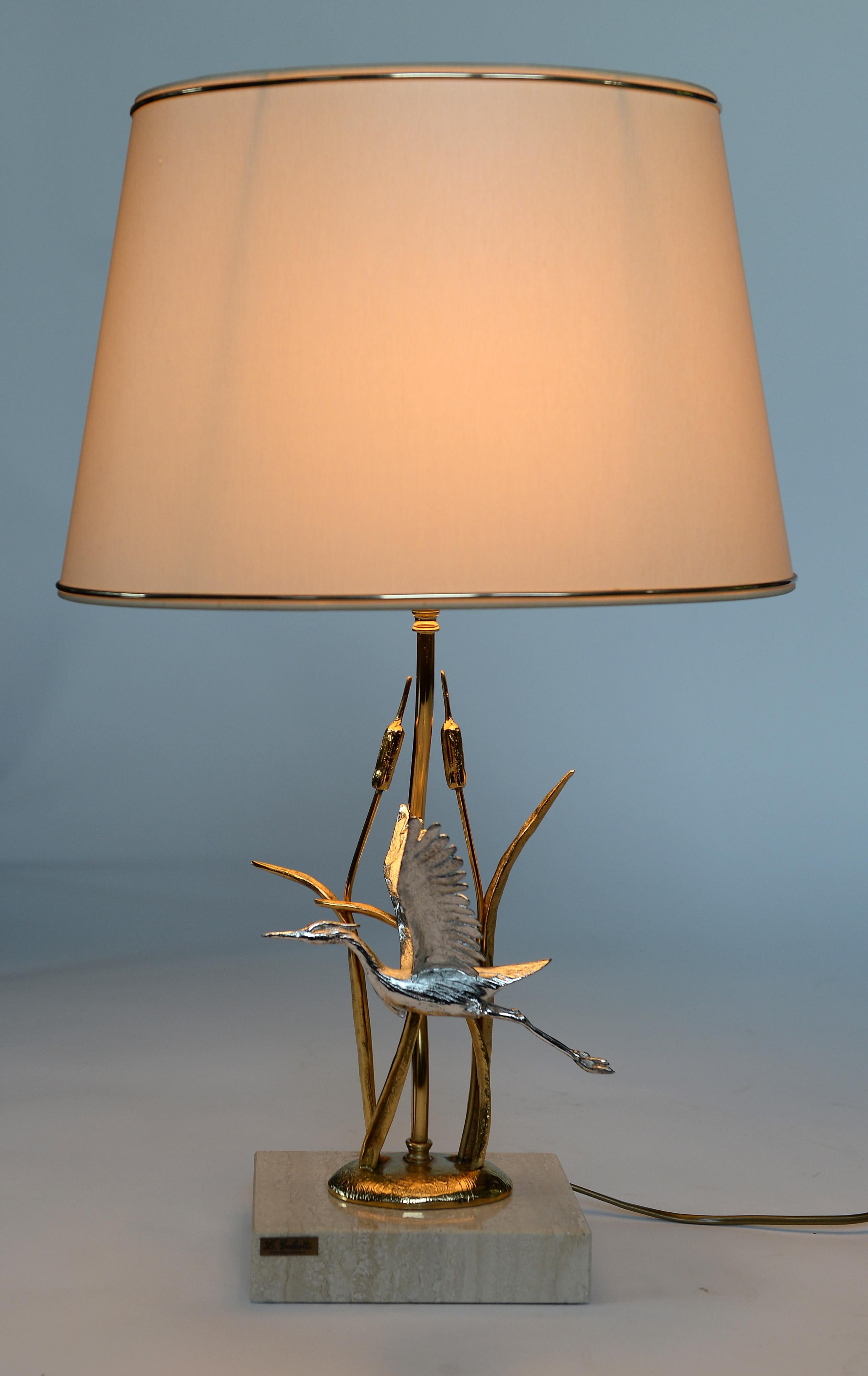 Vintage natural table lamp depicting a a flying heron between wheat.

The brass sculpture is mounted on a travertine stone base, which is typical for italian lamps.

The lamp is labeled and designed by Lanciotto Galeotti for
