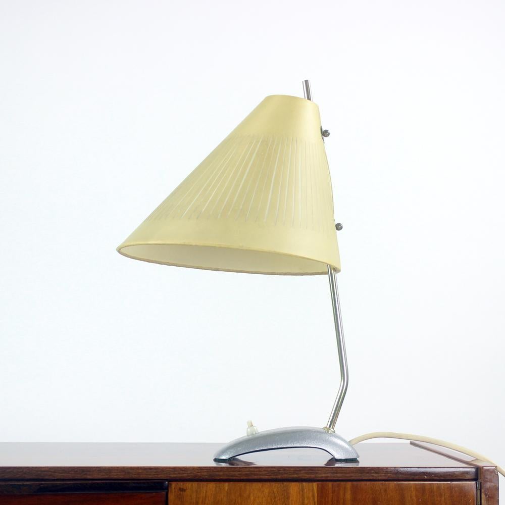 Vintage table lamp produced in Czechoslovakia in 1950s. The design of the lamp show a period between art deco and midcentury modern perion with the original brass rod connecting the base and shield of the light. The base is metal with beautiful