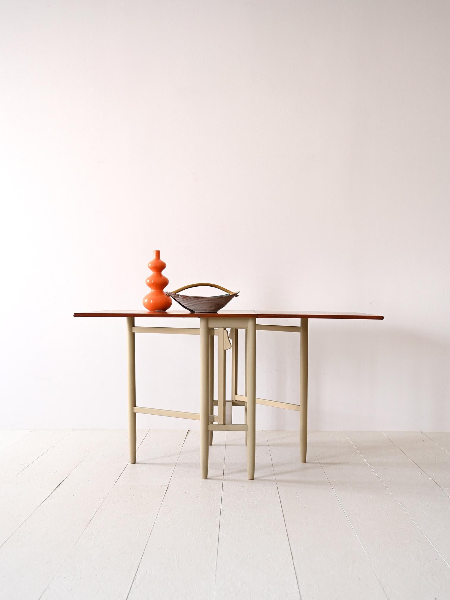 Scandinavian wooden table from the 1960s.

Peculiar Swedish modern antique furniture with teak top and creamy white painted legs.
Ideal for inclusion in a room where space is limited and usage needs may vary.
Consists of a base with long tapered