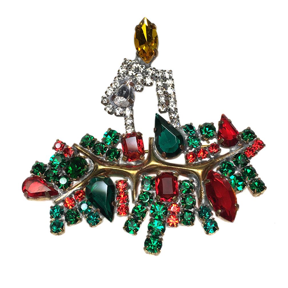 This is a vintage Taboo rhinestone yule candle brooch. This holiday season jewelry has green and red glass/rhinestones decorated around a lit clear rhinestone candle in the center. It has bare brass and heavy soldering on the back which are typical