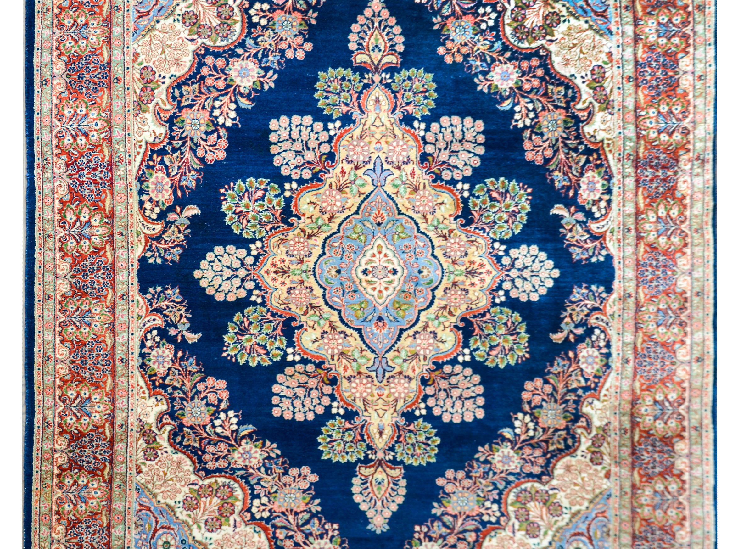 A fantastic 20th century Persian Tabriz rug with a large central floral diamond medallion woven in myriad colors including yellow, green, crimson, pink, and pale indigo, and all set against a dark indigo background. The borer is stunning with a wide