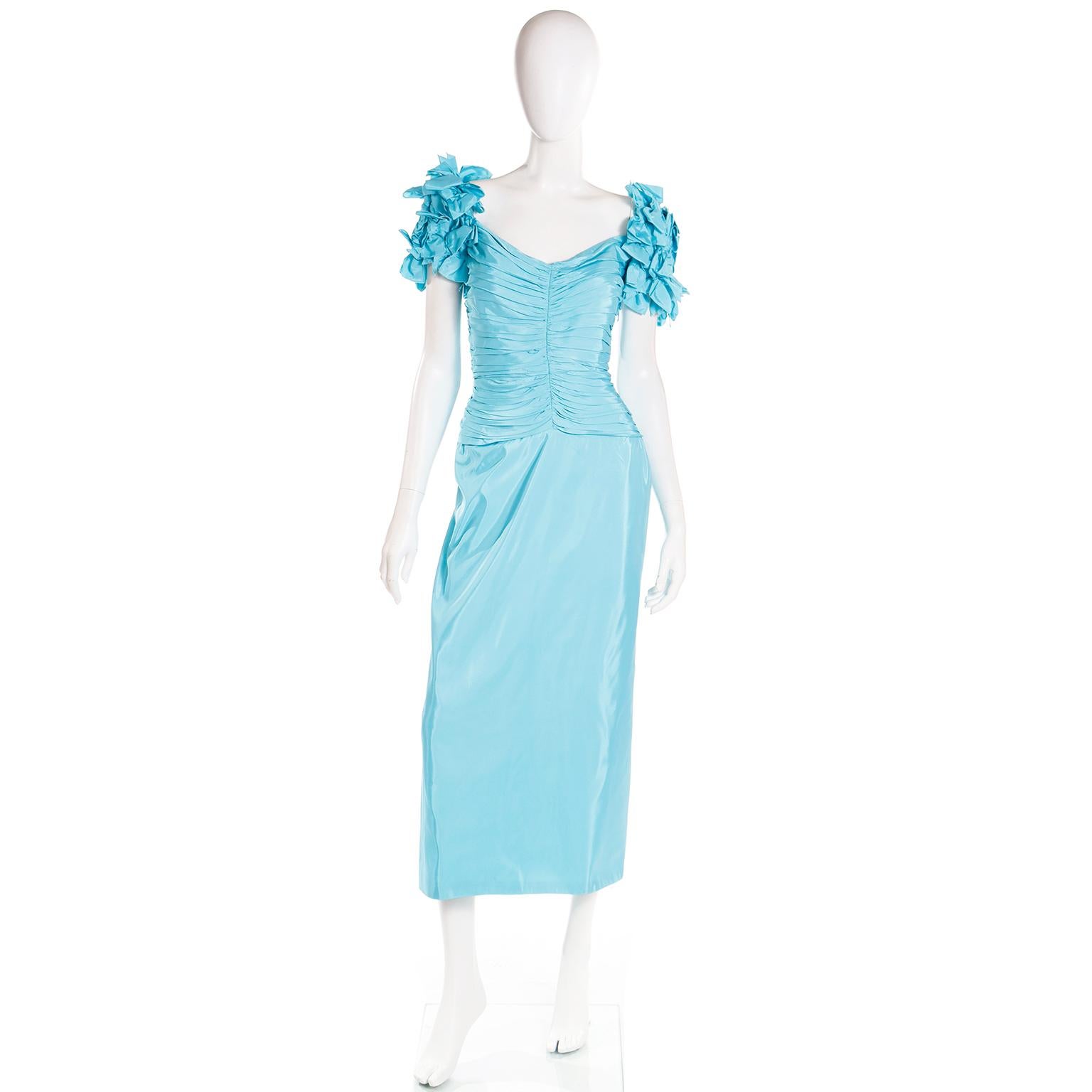 This is a vintage Tadashi evening dress in a pretty blue satin with flattering horizontal ruching from the neckline to the high hip. We love the dramatic sleeves that are covered in little bows! The dress closes with a hidden center back zipper and