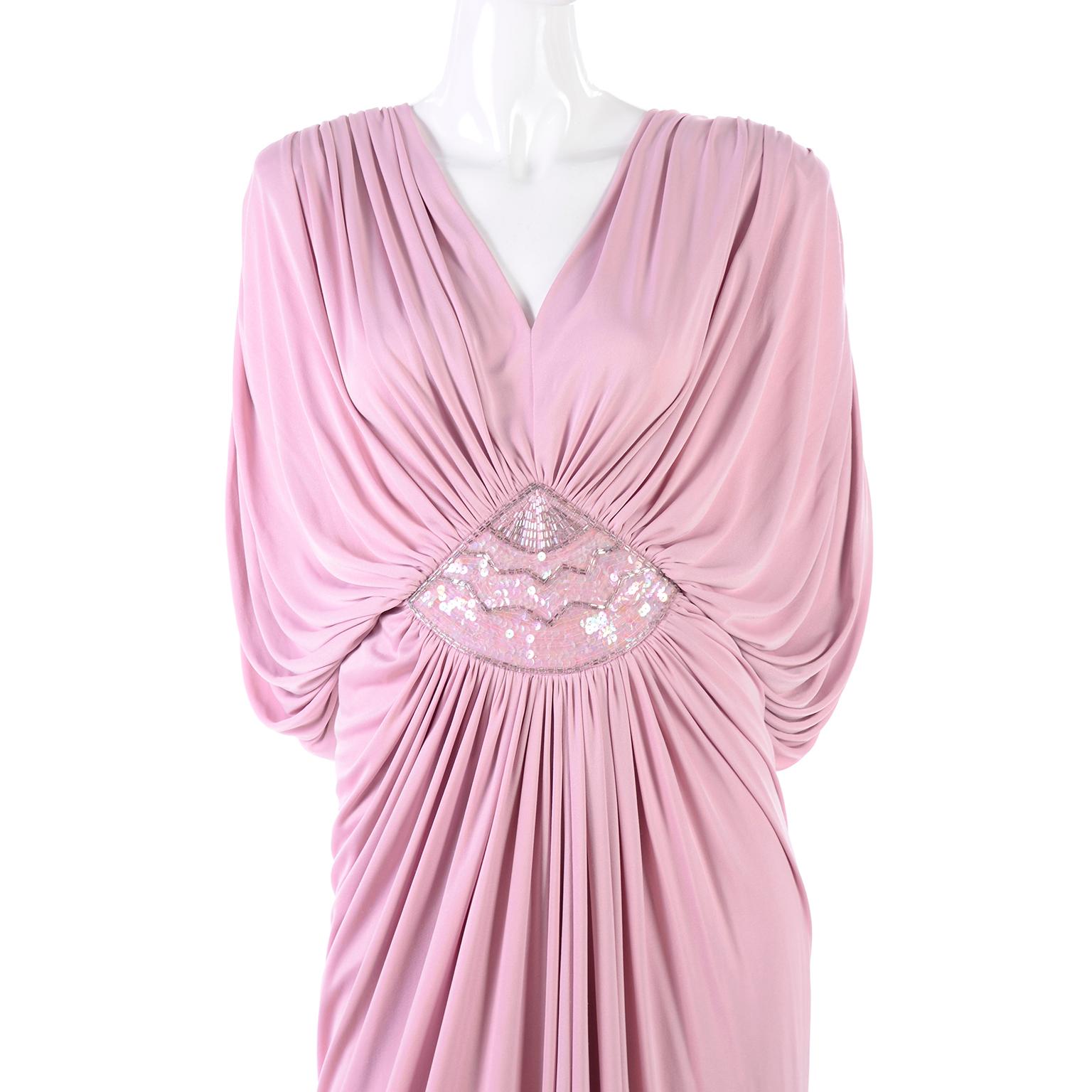 This is a show-stopping Tadashi Shoji evening gown from the early 1980's in a gorgeous draping rose pink/mauve jersey. It has a heavily draped bodice with batwing sleeves and a deep V neck. The drapes attach at the waist and cascade down the front