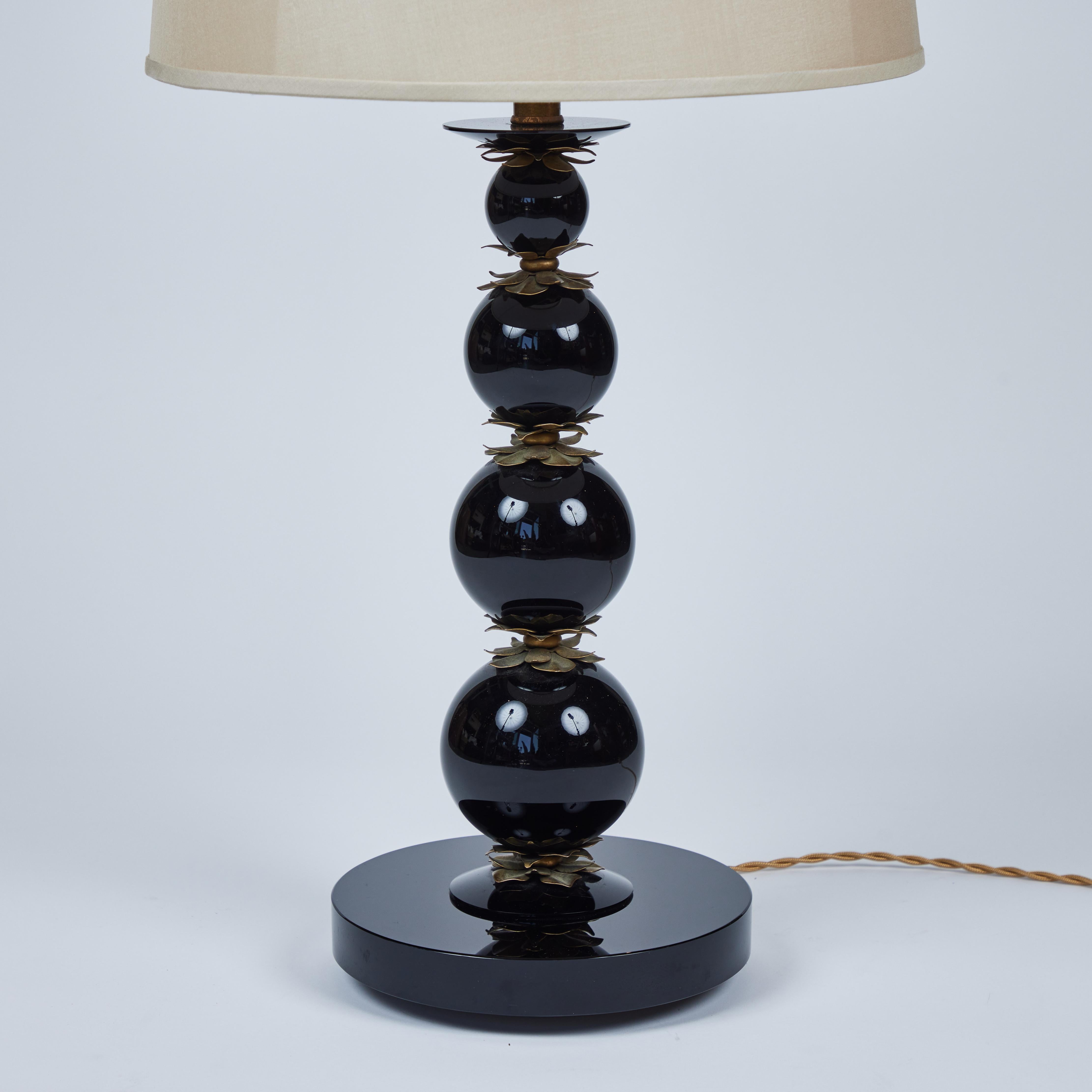 This striking vintage tall black glass table lamp has that eye-catching graduated ball design but each sphere is separated by delicate decorative antique brass flowers with a matching finial that sits on a round flat glass base. It has been paired