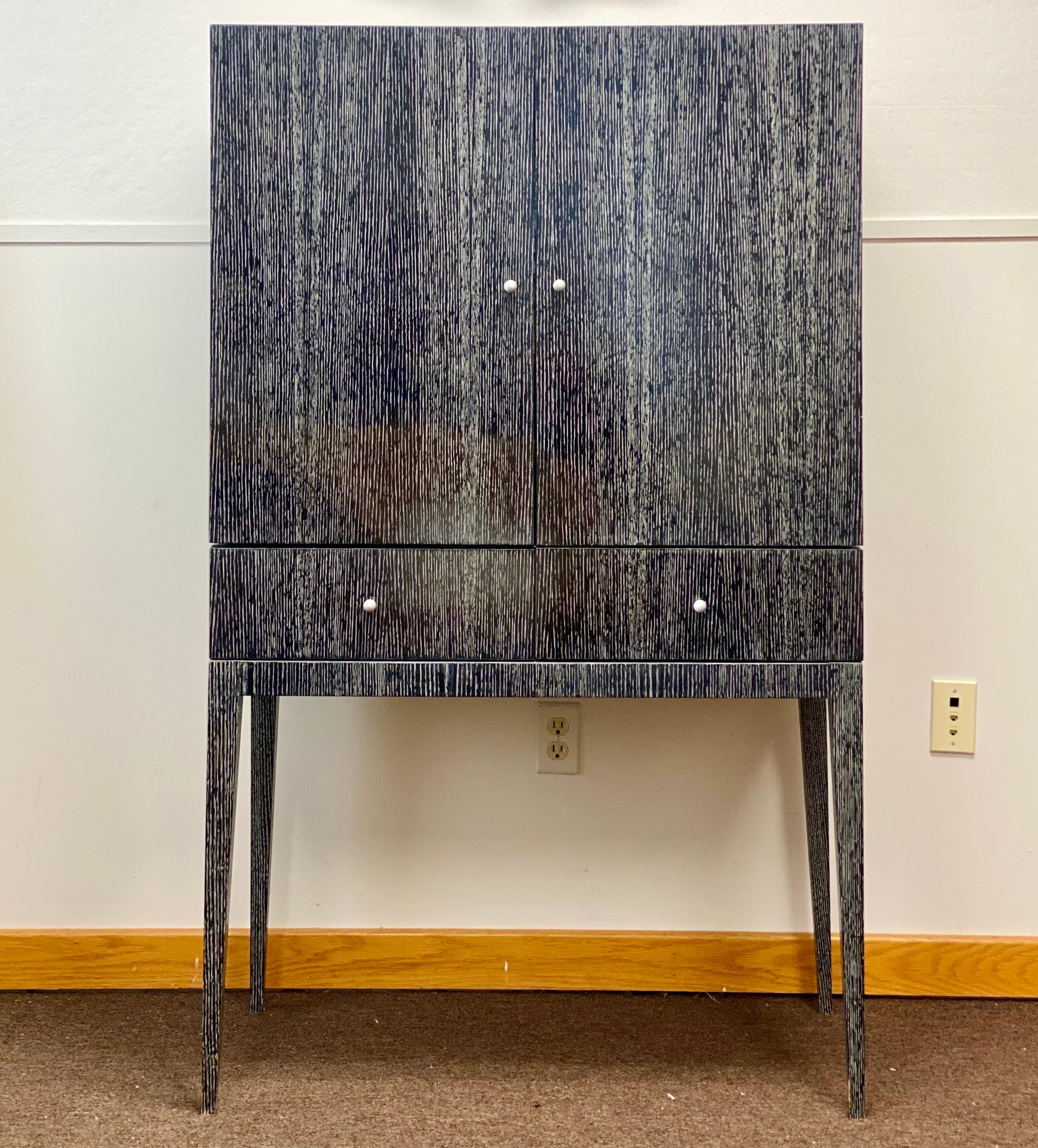 We are very pleased to offer a chic, tall bar circa the 2000s. A deep gray, cerused frame stands tall with two cabinet doors and two bottom drawers that open widely to concealed storage and an abundance of space for a well-stocked bar. This stunning