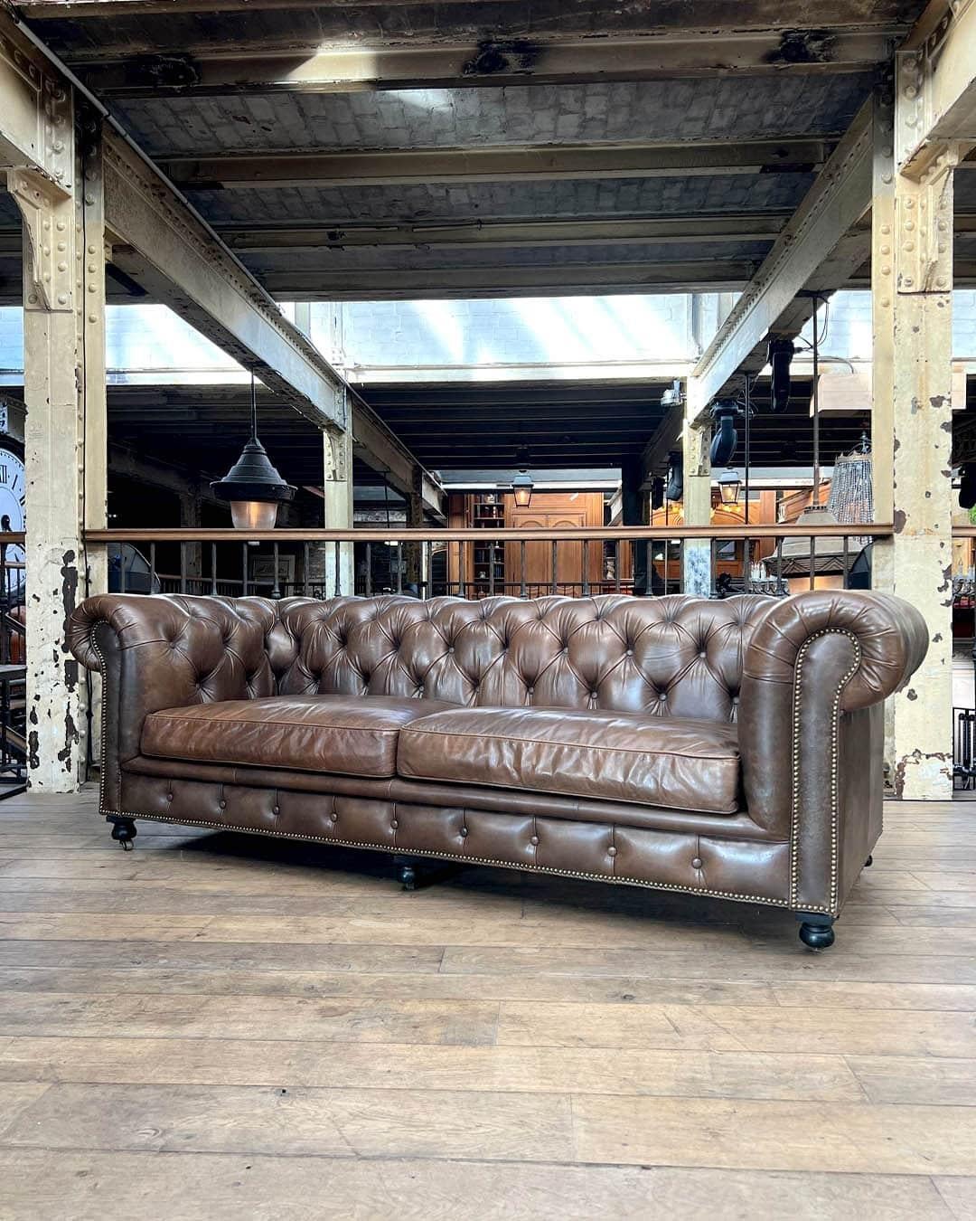 legantes Chesterfield-Sofa mit Polsterung aus patiniertem taupefarbenem Leder, mit klassischer, tiefer Knopfheftung, gerollten Armlehnen und zwei großen Sitzpolstern. Die Vorderkante ist mit dekorativen Messingnägeln verziert, die den zeitlosen