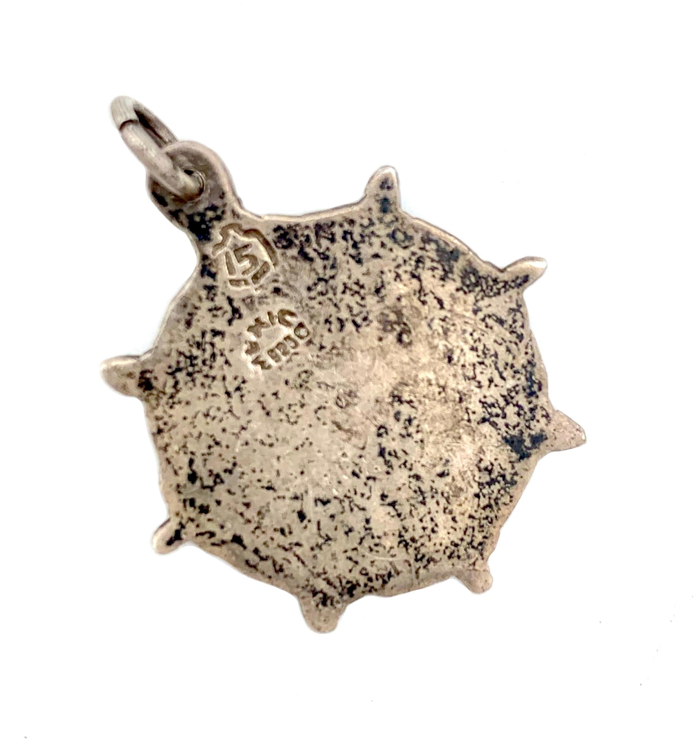 Questo piccolo ciondolo in argento sterling è stato splendidamente inciso con simboli aztechi e una maschera al centro.
Il ciondolo è smaltato con smalto guilloché nei colori rosso, verde, arancione, giallo, bianco e blu.
Sul retro del ciondolo sono