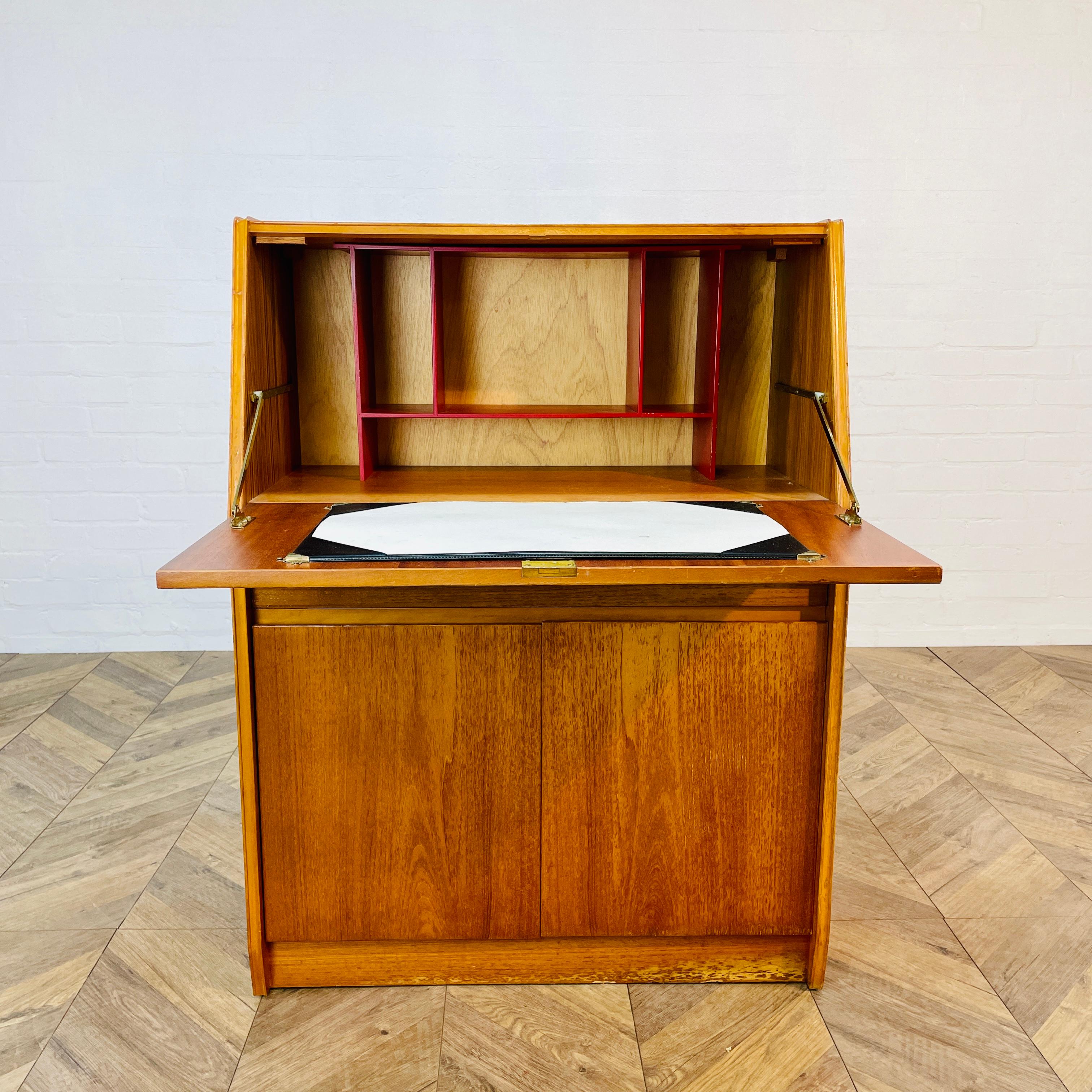 Bureau en teck du milieu du siècle, fabriqué par Remploy - années 1970.

Le bureau comprend un pupitre, un tiroir simple et deux portes de placard.

Le meuble présente des signes d'usure dans les coins, conformément à son âge et à son utilisation,