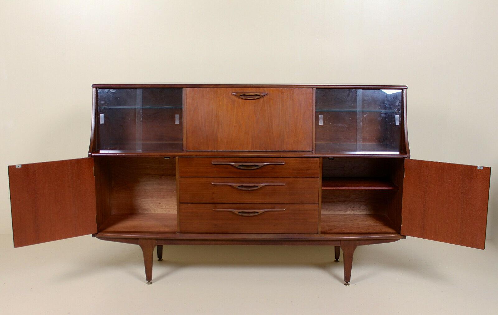 Mid-20th century, (circa 1970) teak glazed cocktail sideboard. The fall flap enclosed mirrored interior and lighting and flanked by sliding glazed doors enclosed glass shelving. Fitted three long drawers below with solid interiors flanked by