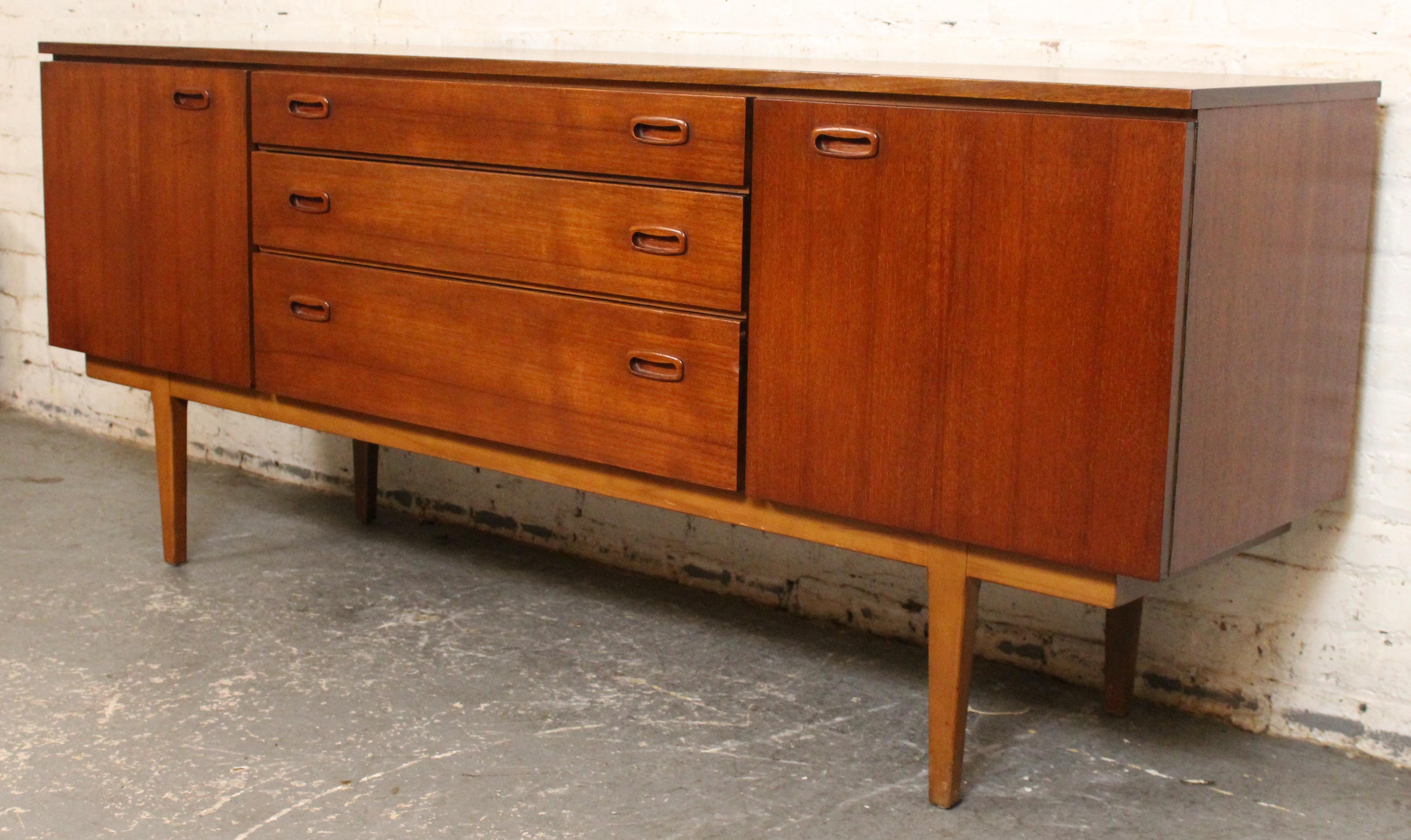 Élégant buffet en teck de fabrication britannique présentant des lignes épurées, des poignées encastrées et de nombreux rangements avec tiroirs et armoires. Design/One Scandinavian avec un grain de bois riche et un profil minimaliste - parfait pour
