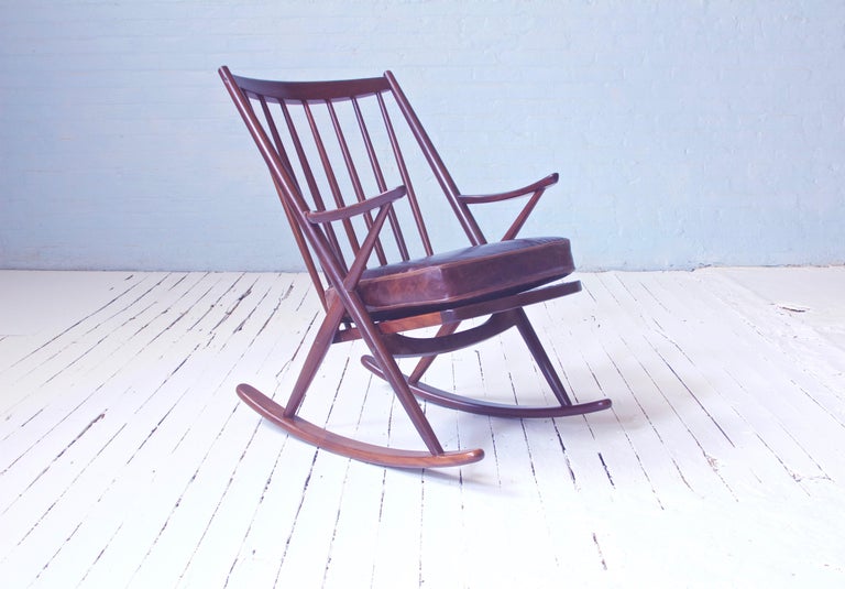 Whimsical and comfortable Frank Reenskaug spindle back rocking chair in gorgeous old growth teak with vinyl cushion. Striking geometry and bold trompe l'oeil joinery really set this form apart from your typical rocker. Reenskaug made a daring and