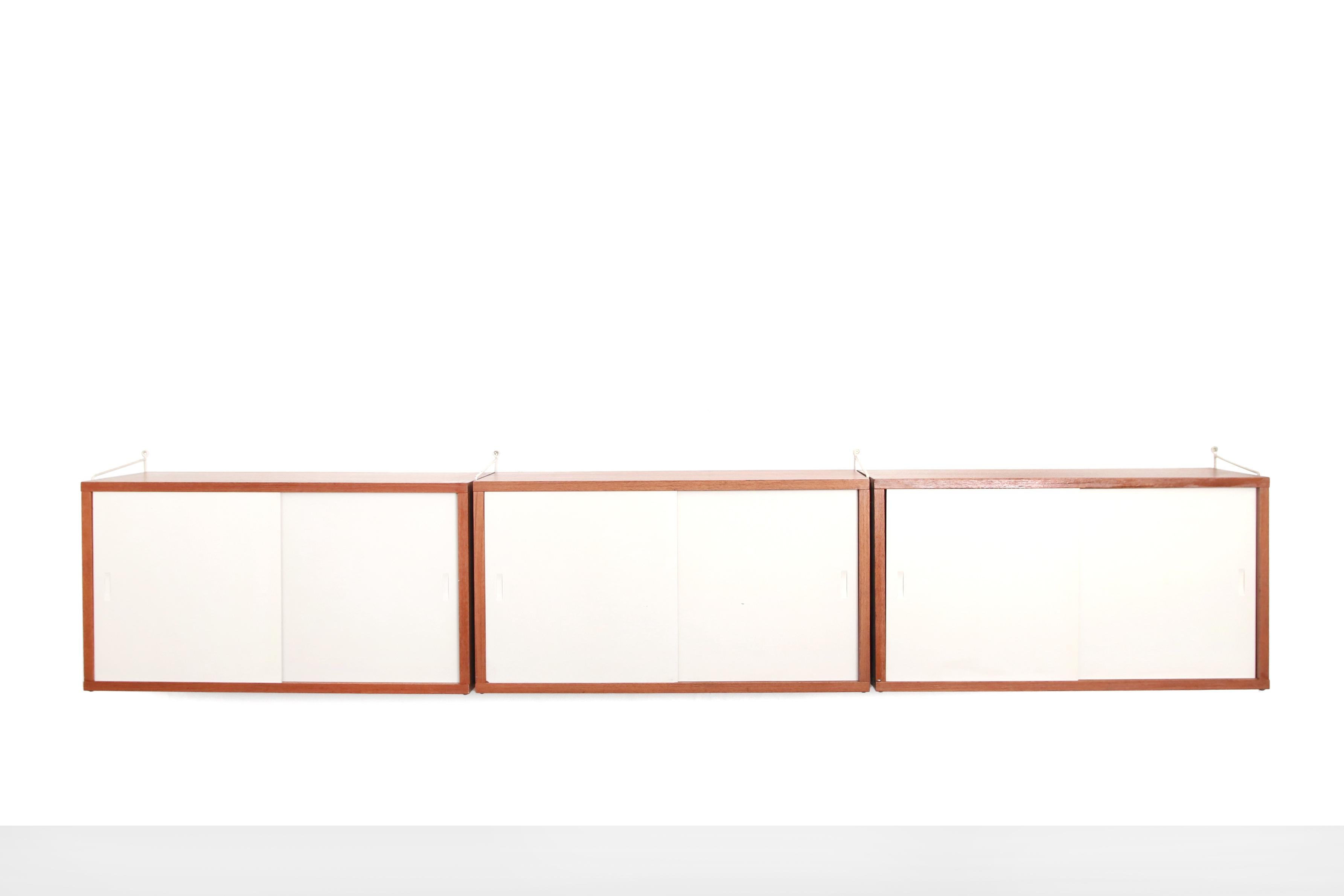 Beautiful string wall rack / sideboard designed by Nisse Strinning. This rack is a real vintage model from the late 1950s-early 1960s. This system consists of 4 white uprights and 3 teak cabinets with white sliding doors. Wonderful to use as a