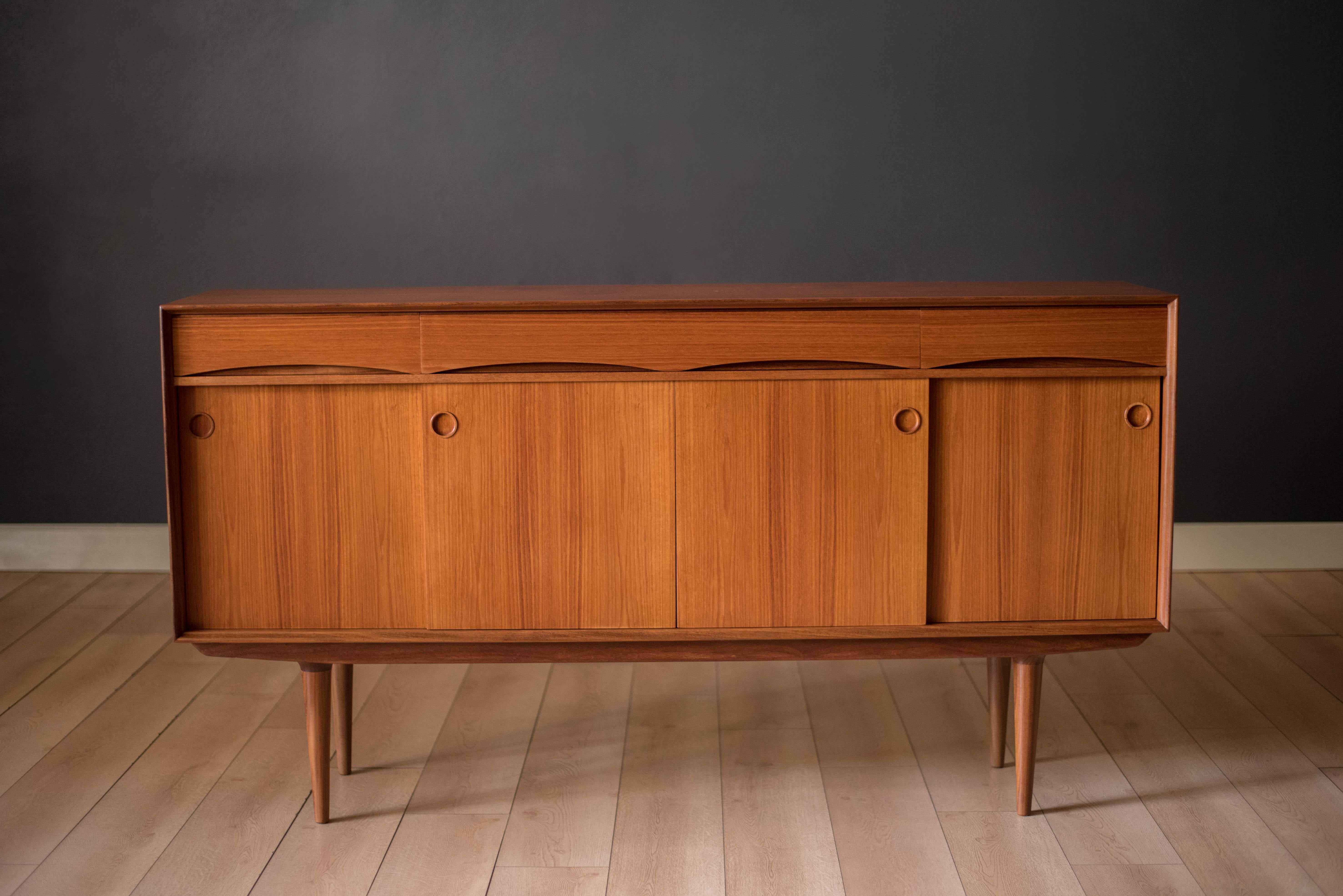 Mid-Century Modern sideboard credenza in teak manufactured by Gustav Bahus, Norway. This versatile piece features three drawers with unique inset handles and sculptural tall legs. Features plenty of storage space including three open cabinets