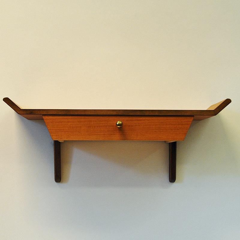 A lovely little teak shelf for any wall produced by AB Nybrofabriken, Fröseke, Sweden, 1960s. Beautiful sculpted top with a little drawer under. Brass knob handle. Good vintage condition and labeled by manufacturer.
Measures: 20 cm H x 50 cm W x 18