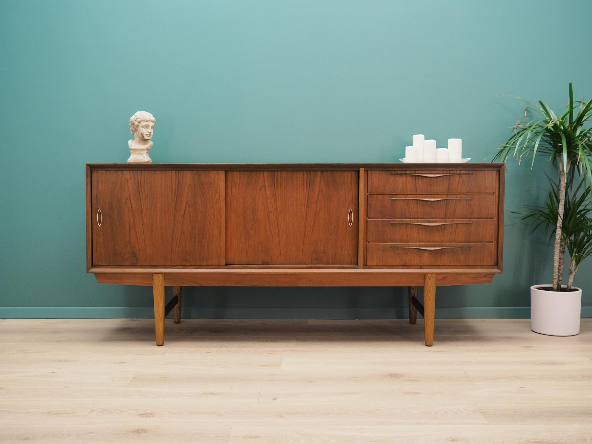 Fantastic sideboard from the 1960s-1970s. Scandinavian design, minimalist form. Furniture is covered with teak veneer, legs are made of solid teak wood. Sideboard has four stylish drawers and a spacious shelf behind a sliding door. Preserved in good
