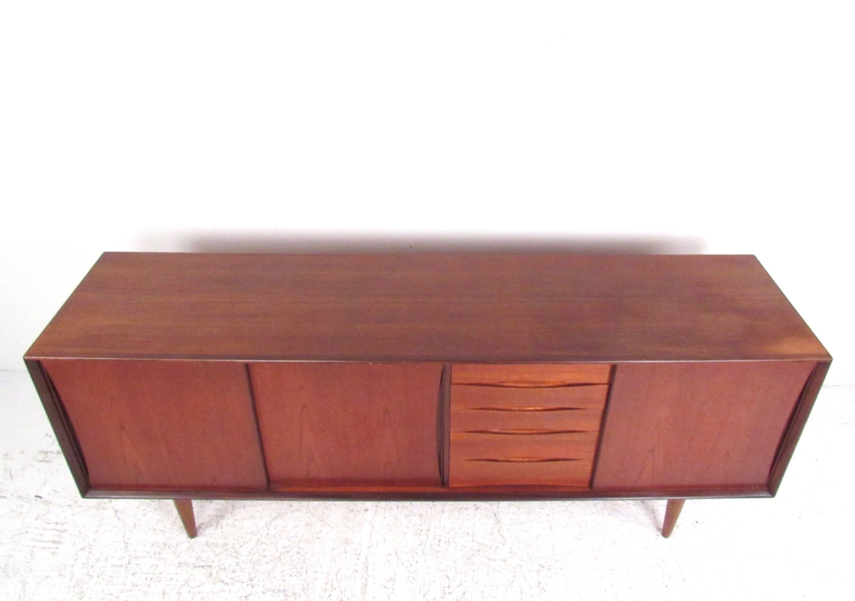 This stylish Scandinavian Modern sideboard features rich Danish teak finish and sturdy midcentury construction. Sculpted drawer pulls and sliding doors add to the Arne Vodder style of this vintage storage piece and make it a striking addition to