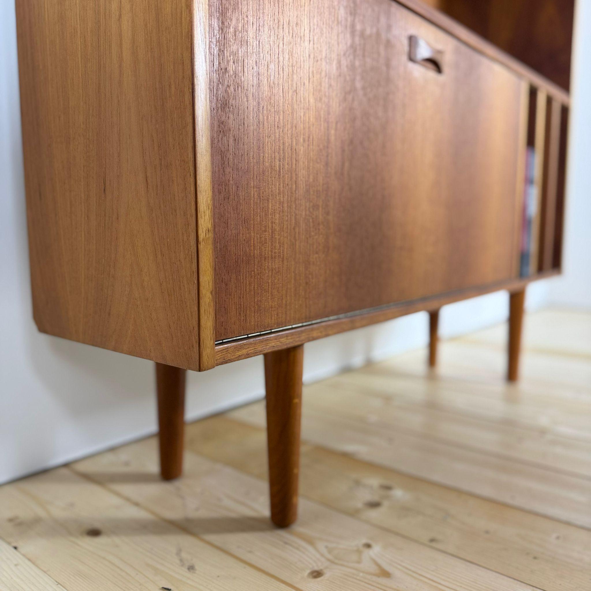 Trasforma il tuo spazio con questa iconica libreria porta vinili in teak, un autentico pezzo danese degli anni '60 di Calusen e Spazio. L'anta a ribaltina nasconde uno Spazio bar in perfette condizioni di conservazione, il fulcro di conversazioni e