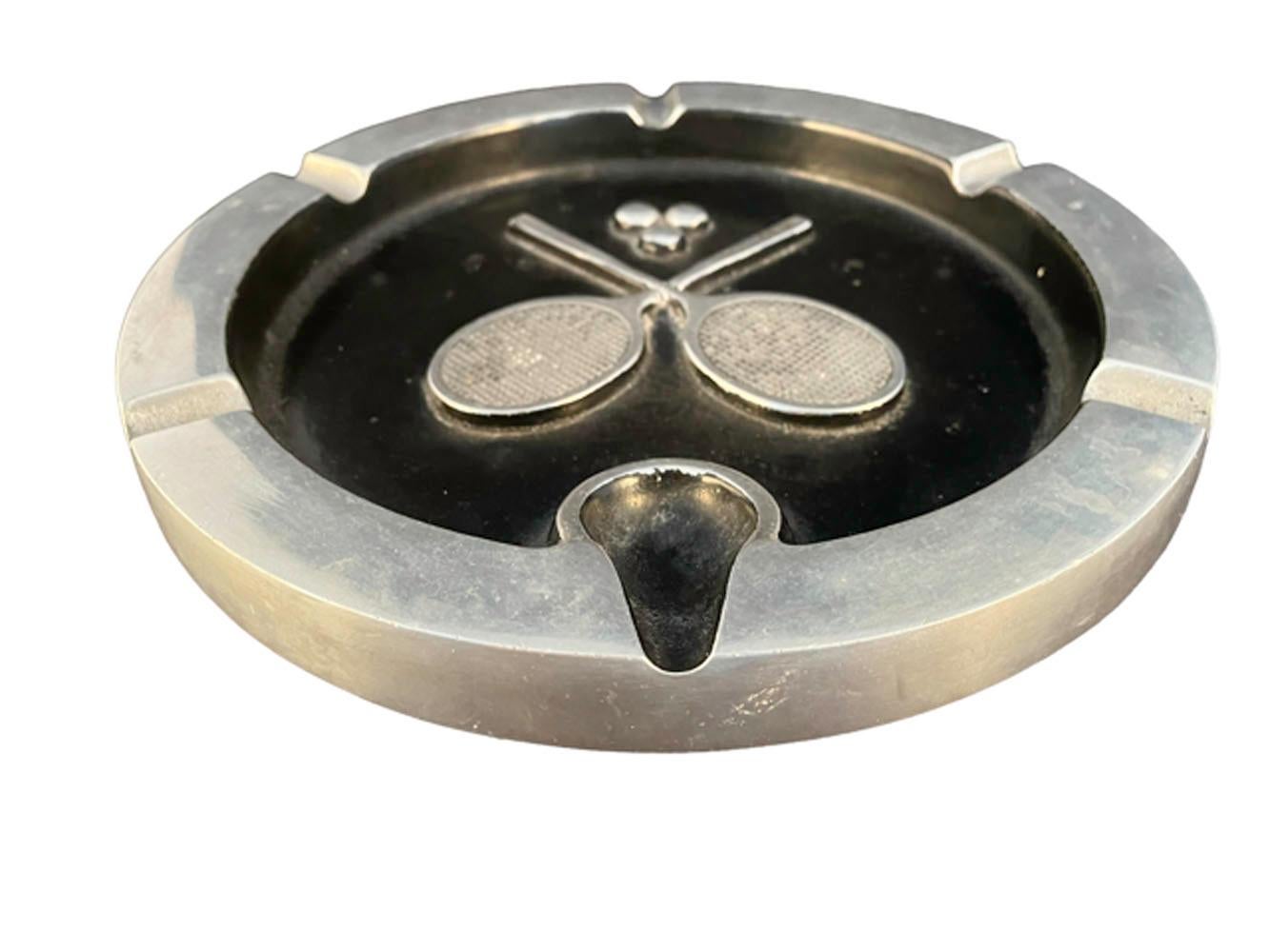 Cast aluminum ashtray of large proportions having raised crossed tennis rackets and balls in the center on a black enameled ground and raised rim with 5 divots for cigars/cigarettes as well as one pipe rest.