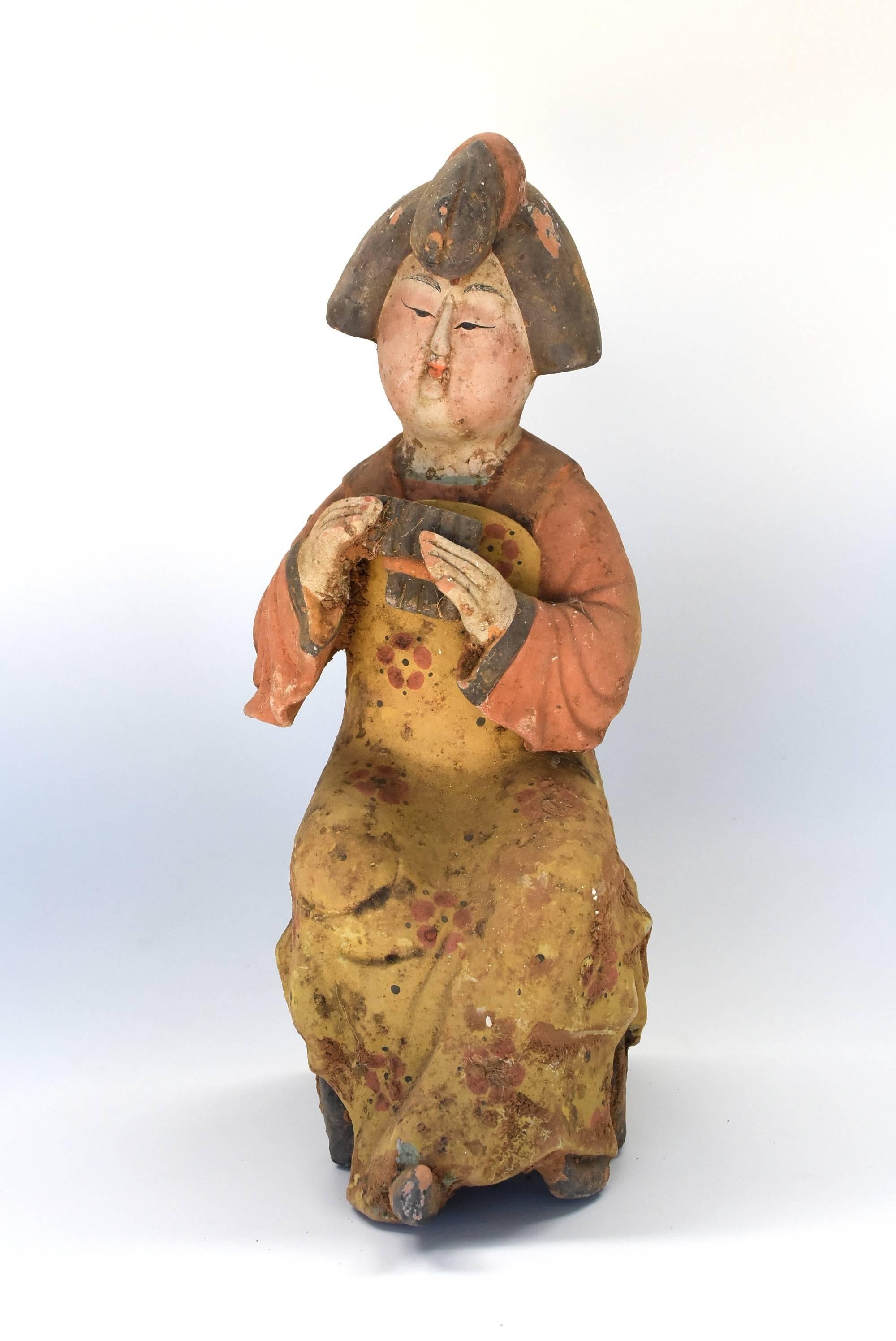A beautiful terracotta court lady in the Tang dynasty San Cai style. This is an older piece from our special collection. The court lady is a musician. She is seated holding a flute. Her hair style, full round face, small mouth, long eyes are all