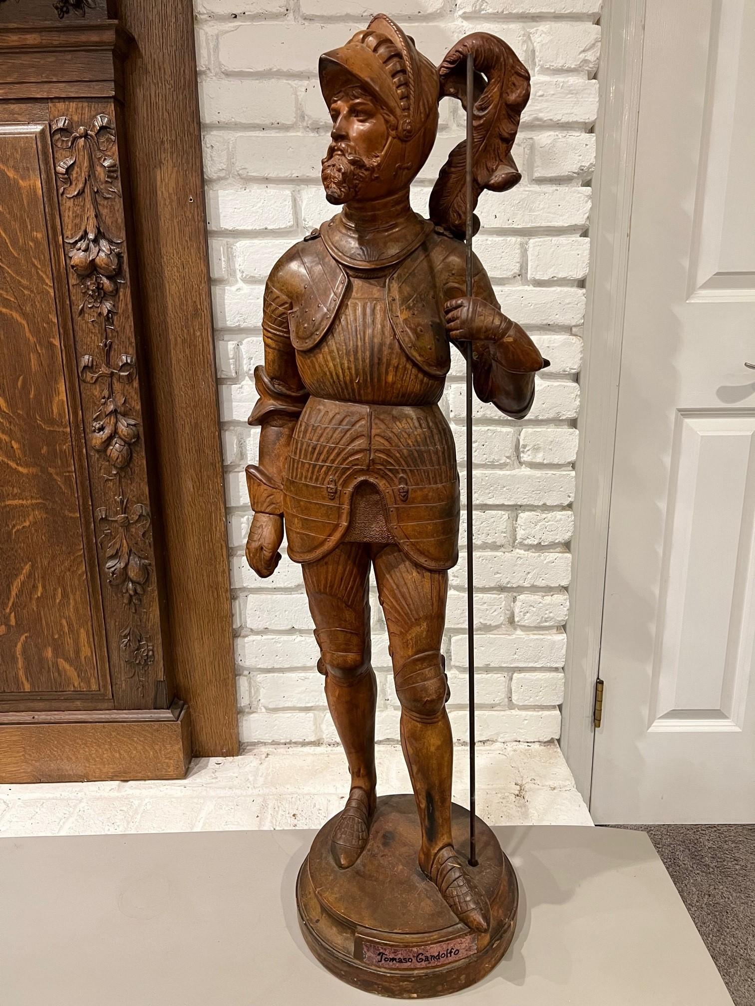 A bold full figure statue of a knight in armor labeled, Tomaso Gandolfo. The Knight I believe is one of The Knights Templar a medieval crusading military order of knights who lived like monks. The Knights Templar were an elite fighting force of