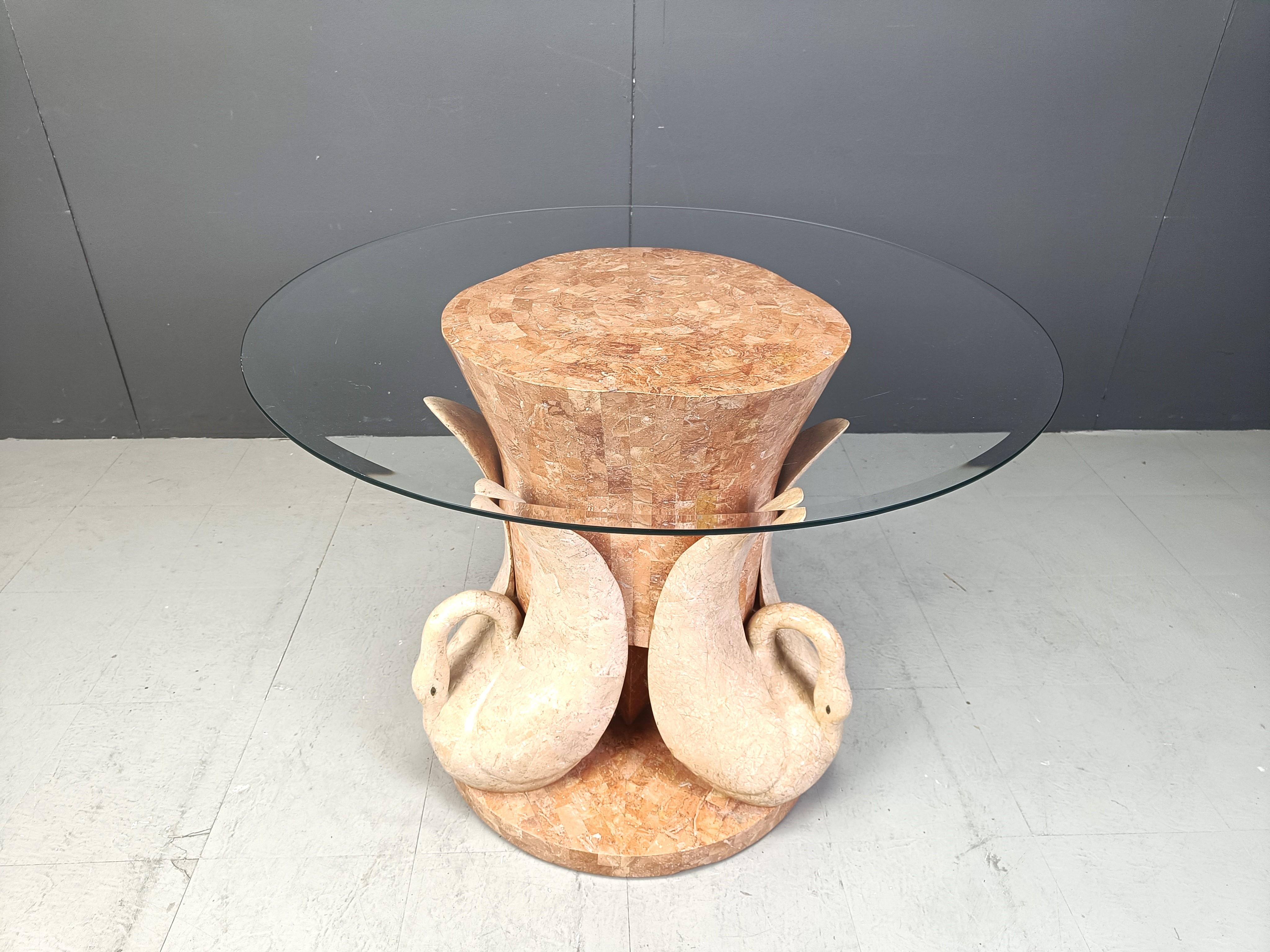 Sculptural tesselated stone swan dining table or centre table.

It features a nice sculptural base featuring three swans and a red tesselated stone base finished with a clear oval glass top.

We can provide any glass type and size uppon request so