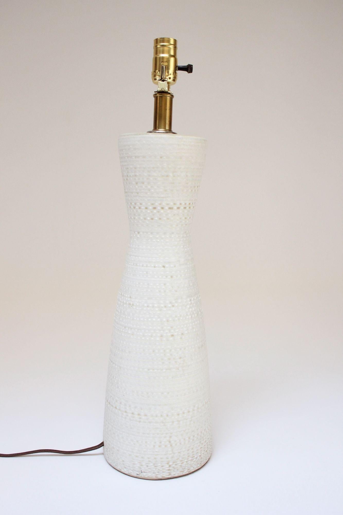 Lampe de table en céramique en forme de sablier en émail texturé/nubby blanc sur beige, conçue dans les années 1960 par Lee Rosen pour Design Technics. Forme sculpturale et moderniste avec une élégante tige et des accents en laiton.
Seule une légère