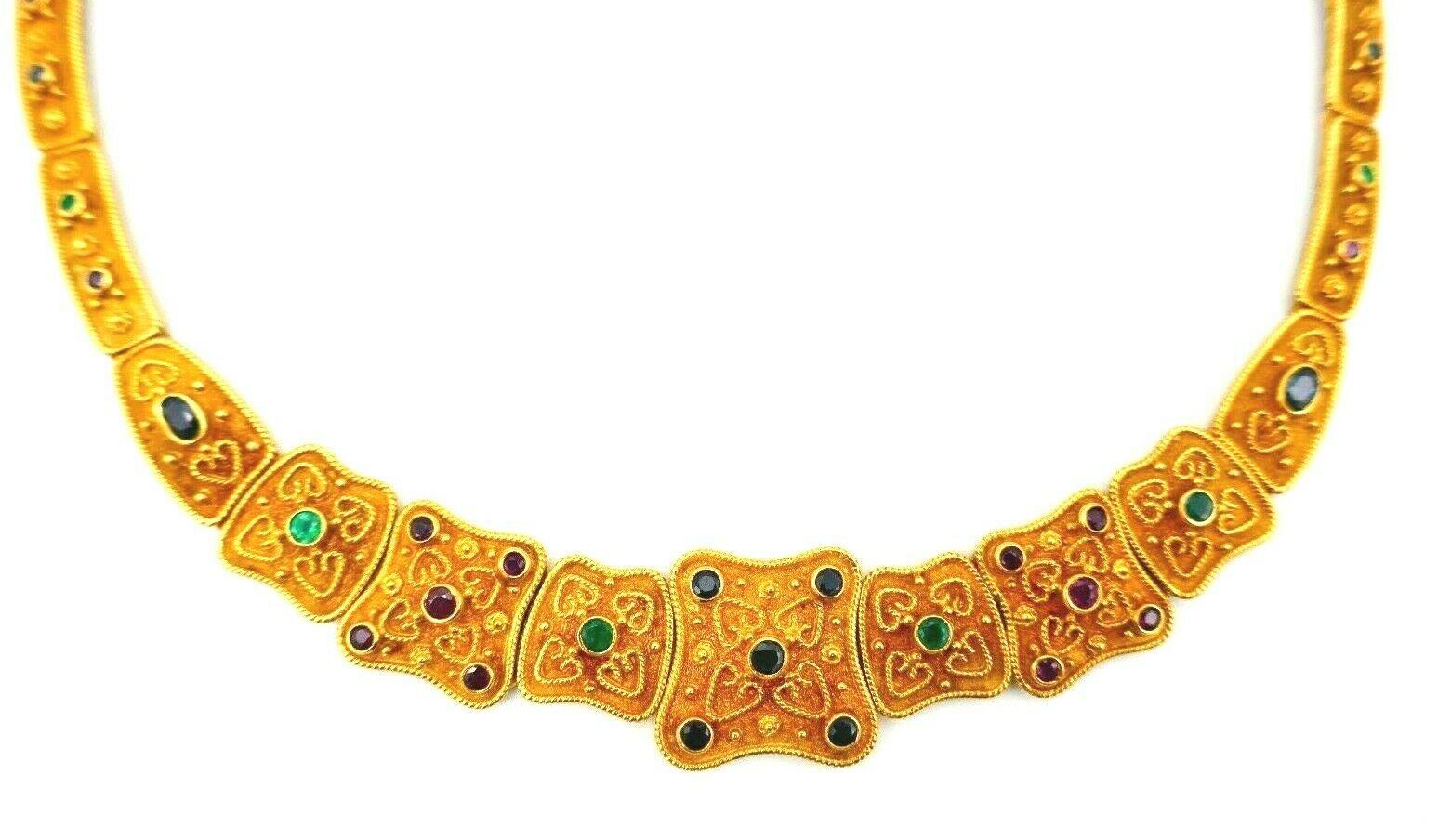 A beautiful collar necklace made of textured 18k yellow gold featuring ruby, emerald and sapphire. 
Comprised of the flat links are connected by hinges. 
Stamped with maker's mark and a hallmark for 18k gold.
Measurements: 16