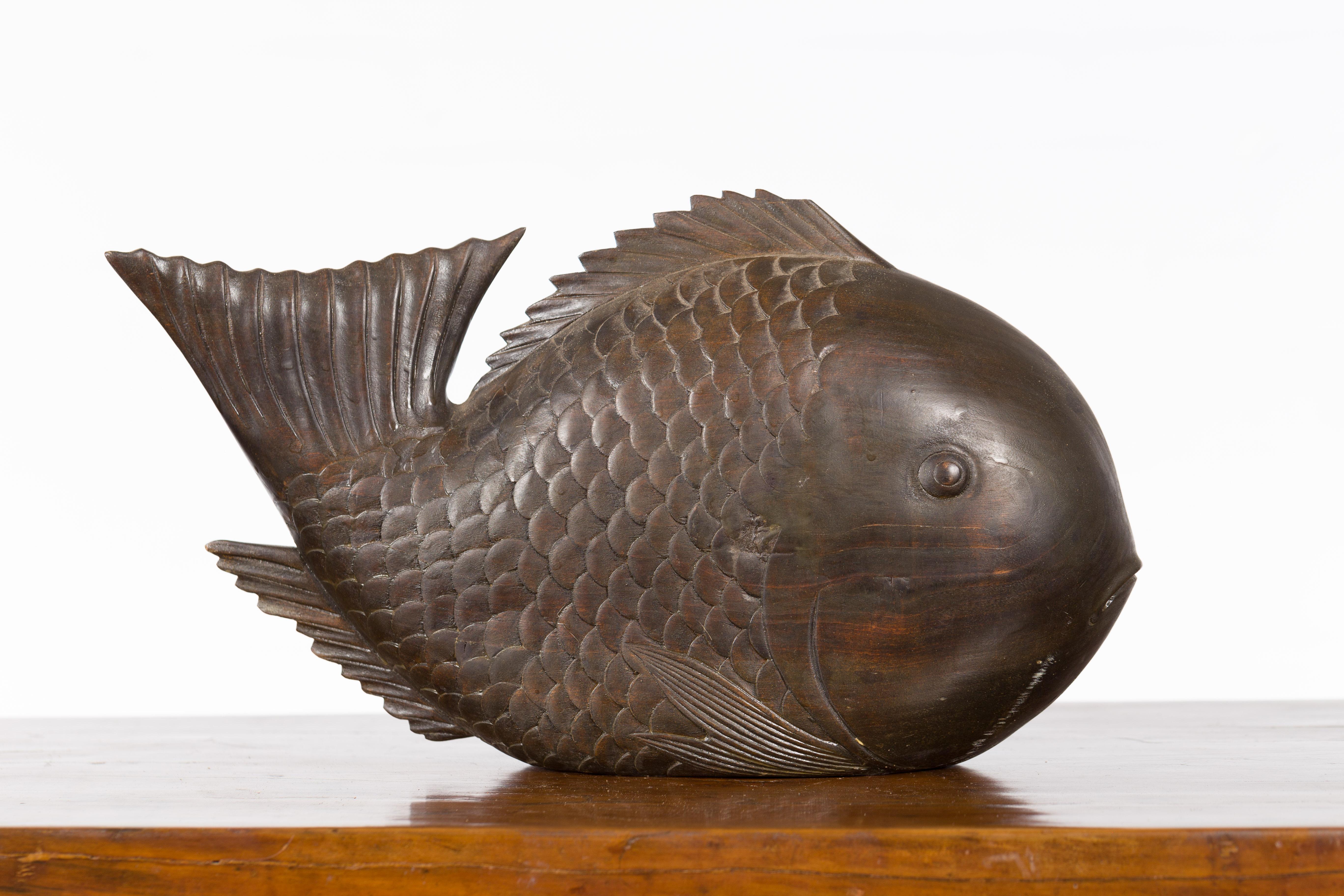 A vintage Thai carved wooden carp from the mid 20th century, with detailed scales and dark patina. We have several available, priced and sold individually. Created in Thailand during the midcentury period, this wooden carp sculpture captures our