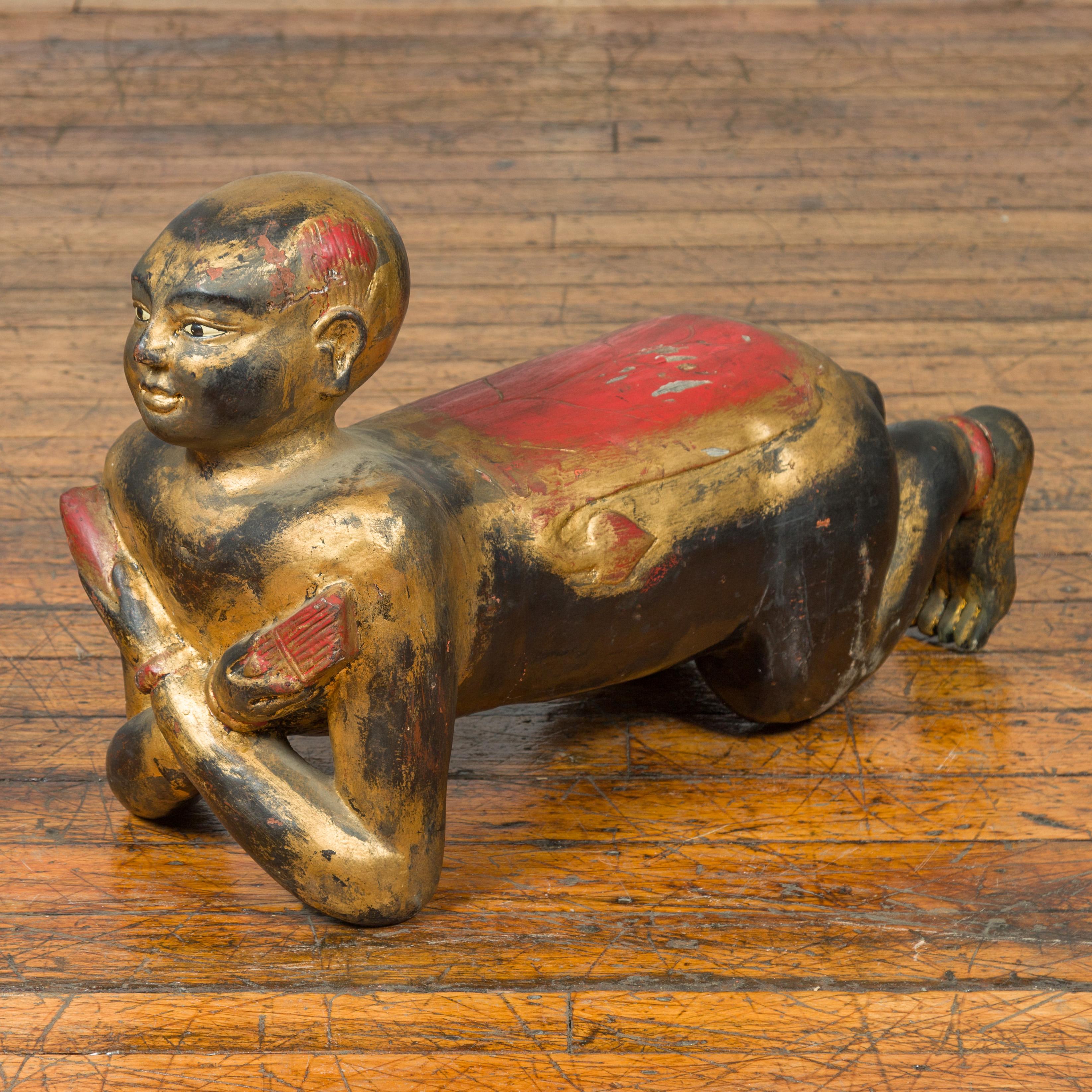 A vintage Thai ceremonial carved giltwood temple guardian sculpture from the mid-20th century, with gold, black and red patina. Crafted in Thailand during the midcentury period, this sculpture features a ceremonial temple guardian, kneeling with his