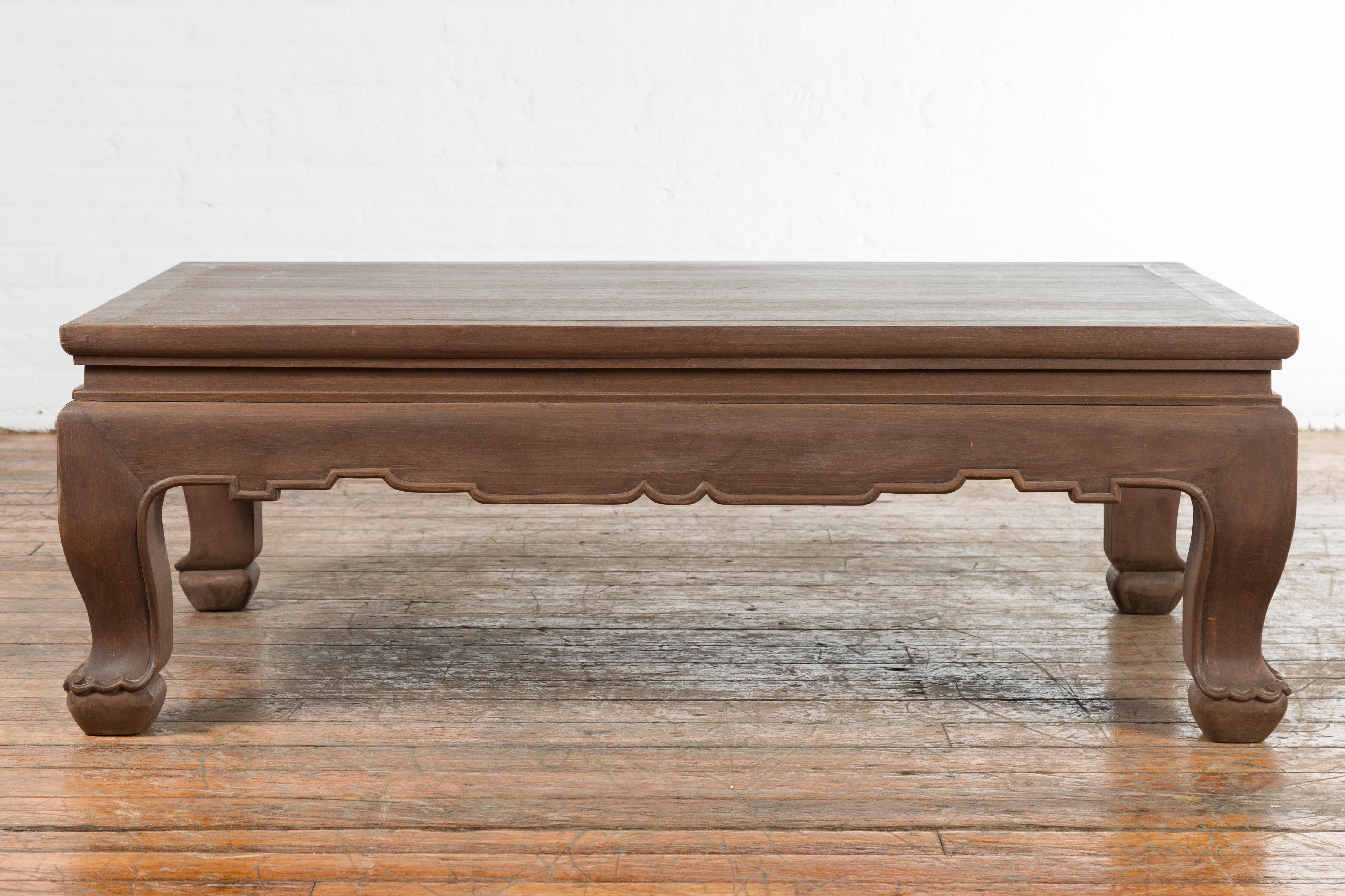 A vintage Thai chow legs coffee table from the mid 20th century, with carved apron and brown patina. Created in Thailand during the midcentury period, this coffee table features a rectangular waisted top sitting above a symmetrically carved apron.