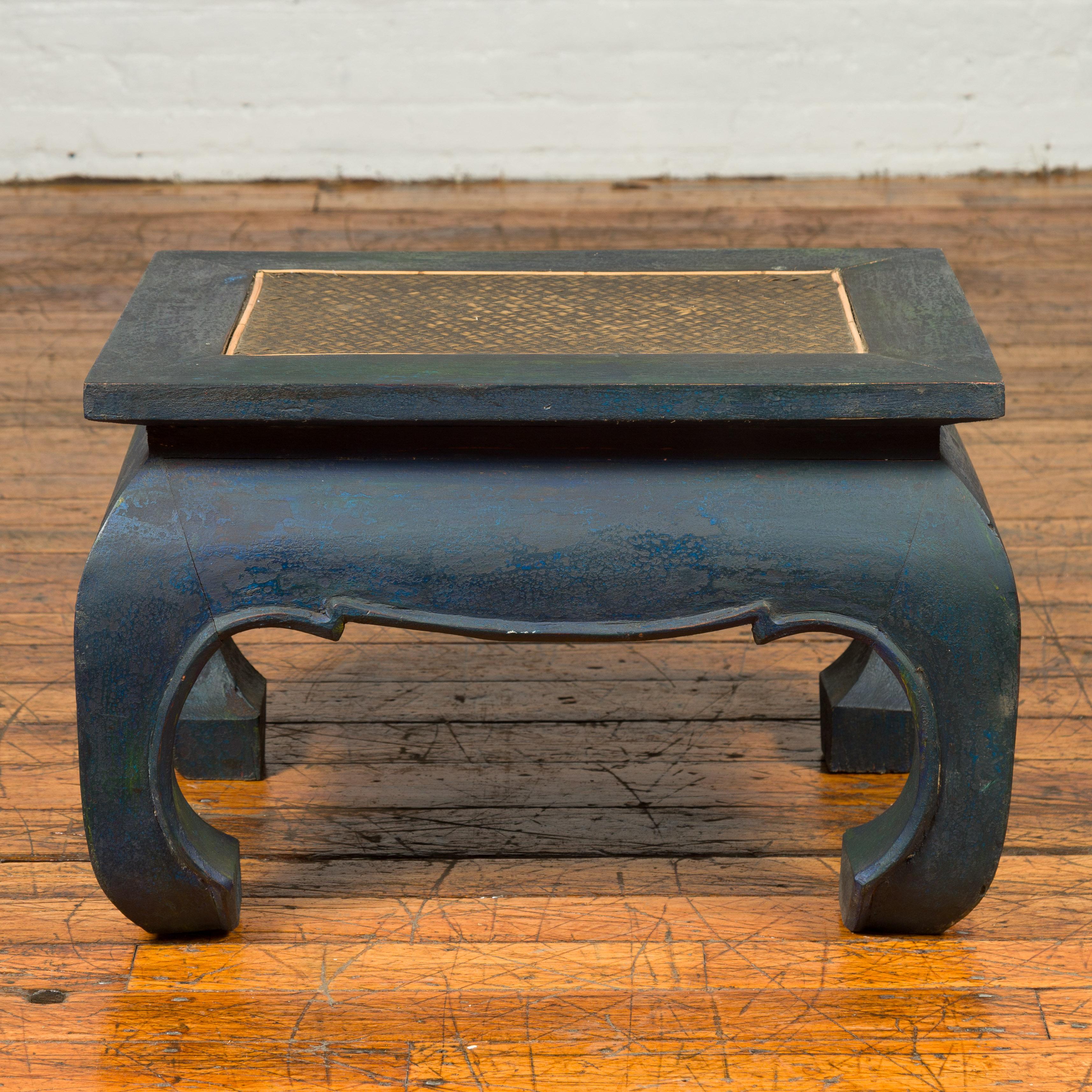 A vintage Thai waisted cocktail table with distressed patina, rattan inset and chow legs. Featuring an eye-catching dark blue distressed patina and Ming style lines, this cocktail table features a rectangular top with rattan inset, sitting above a