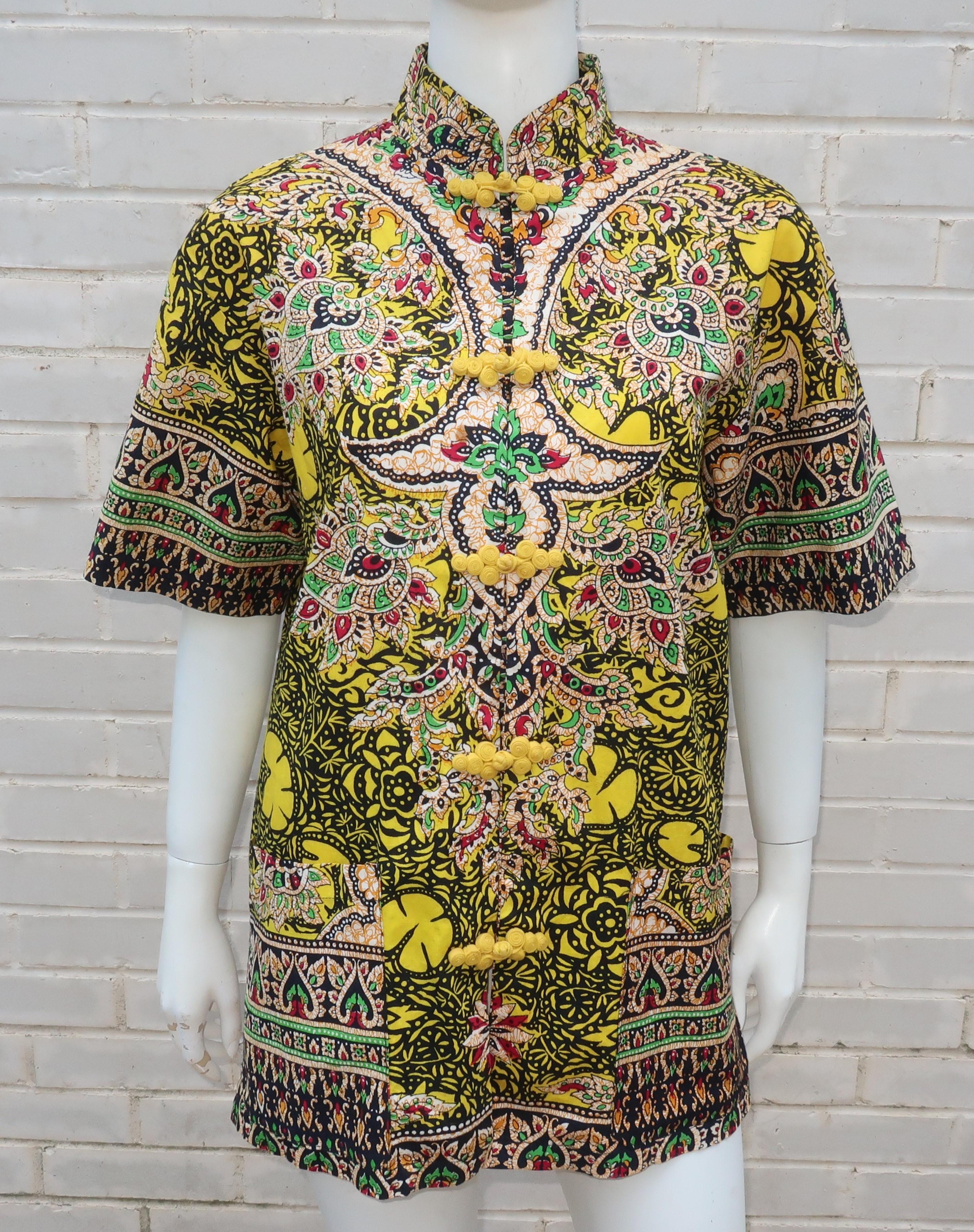 A Mandarin style top made in Thailand from a colorful cotton fabric with a traditional Thai print incorporating shades of bright yellow, green, red, orange, white and black.  The short sleeved silhouette has the details of a jacket with side vents