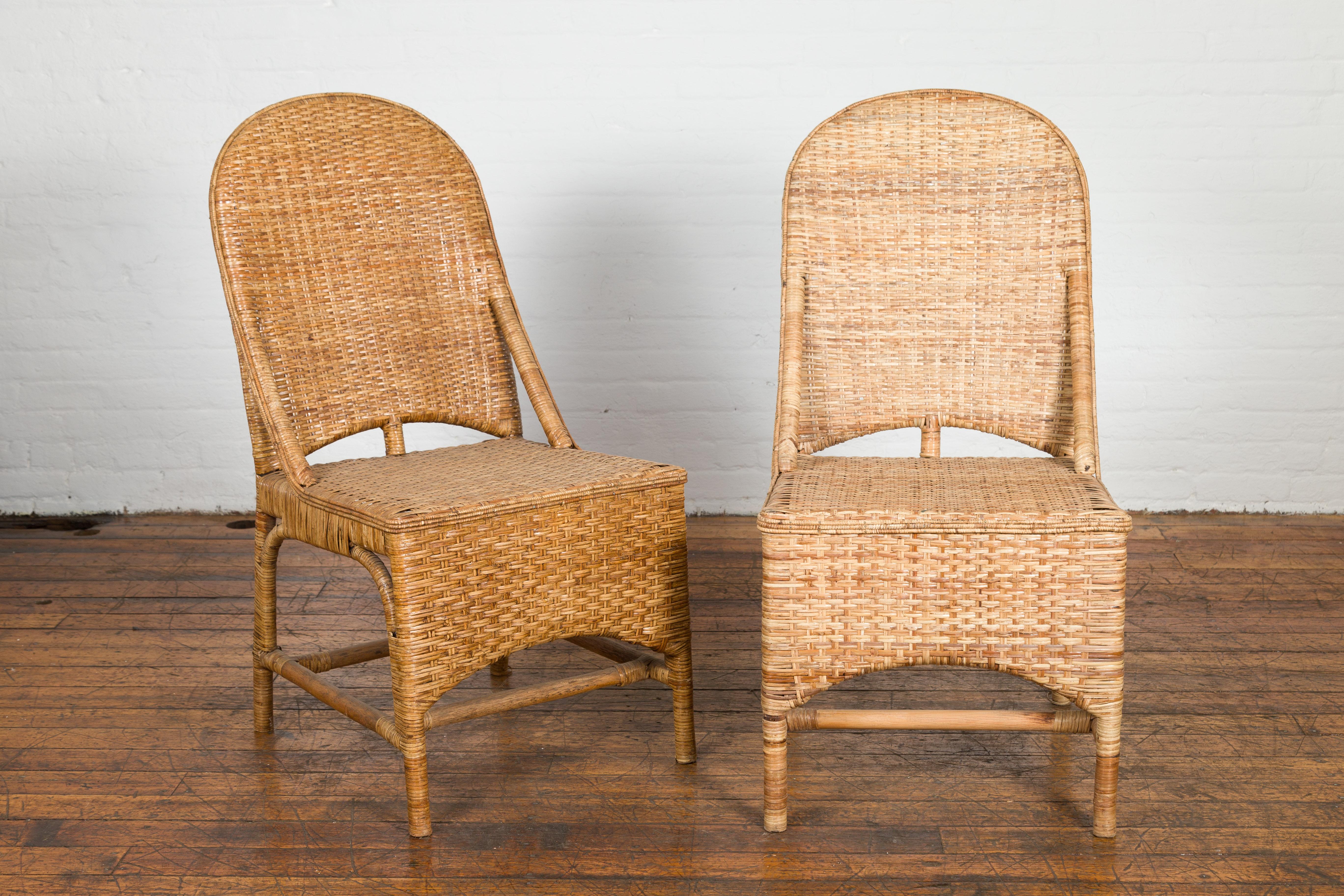 Two vintage Country style Thai hand woven rattan chair from the mid 20th century, with arching backs and H-Form cross stretchers. Embrace a fusion of functionality and earthy aesthetics with these vintage, mid-20th-century Thai rattan chairs.