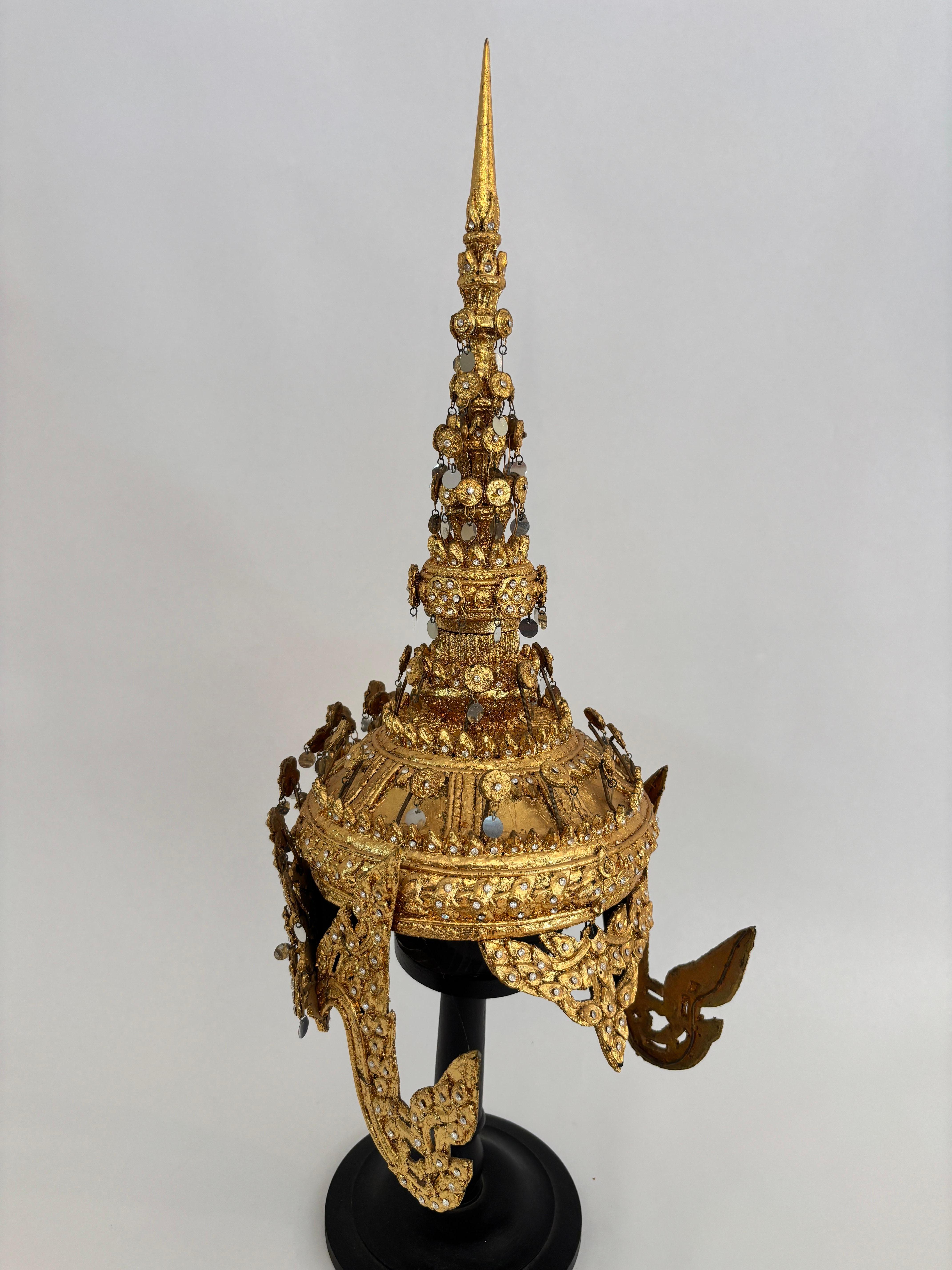 Copricapo cerimoniale dorato thailandese d'epoca con intarsi a specchio, metà del XX secolo, montato su supporto
Un ornato copricapo cerimoniale thailandese (corona di danza Chada o Khon), tradizionalmente indossato nelle esibizioni di danza