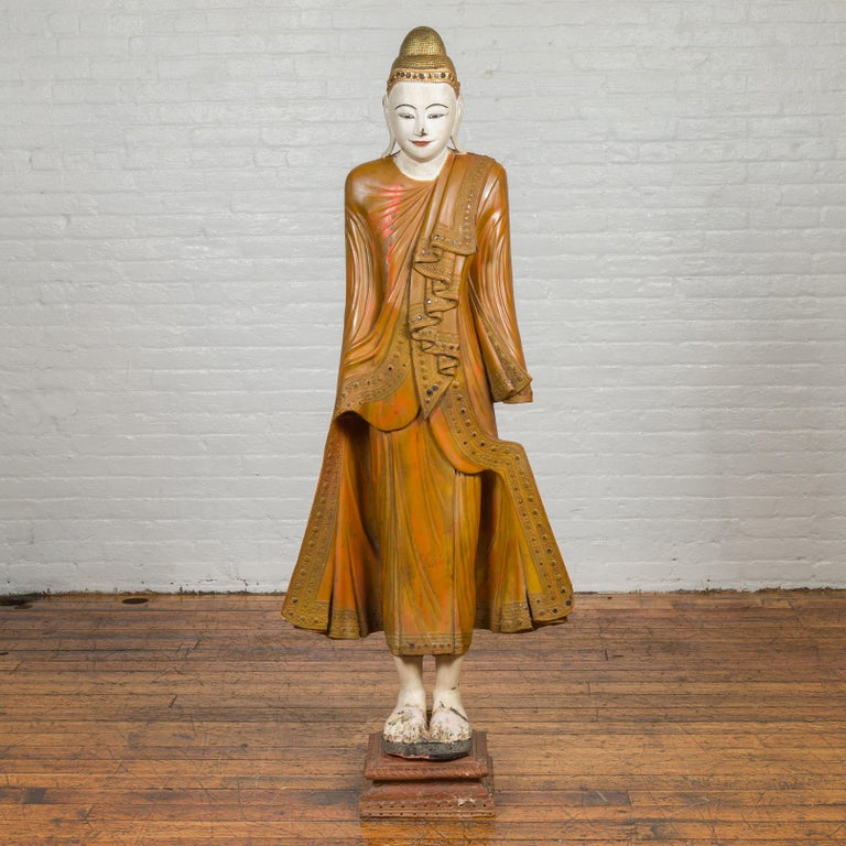 A vintage Thai hand painted and carved wooden standing Buddha sculpture from the mid-20th century, in mandalay style. Crafted in Thailand during the midcentury period, this standing Buddha presents a gentle facial expression in the Mandalay style.