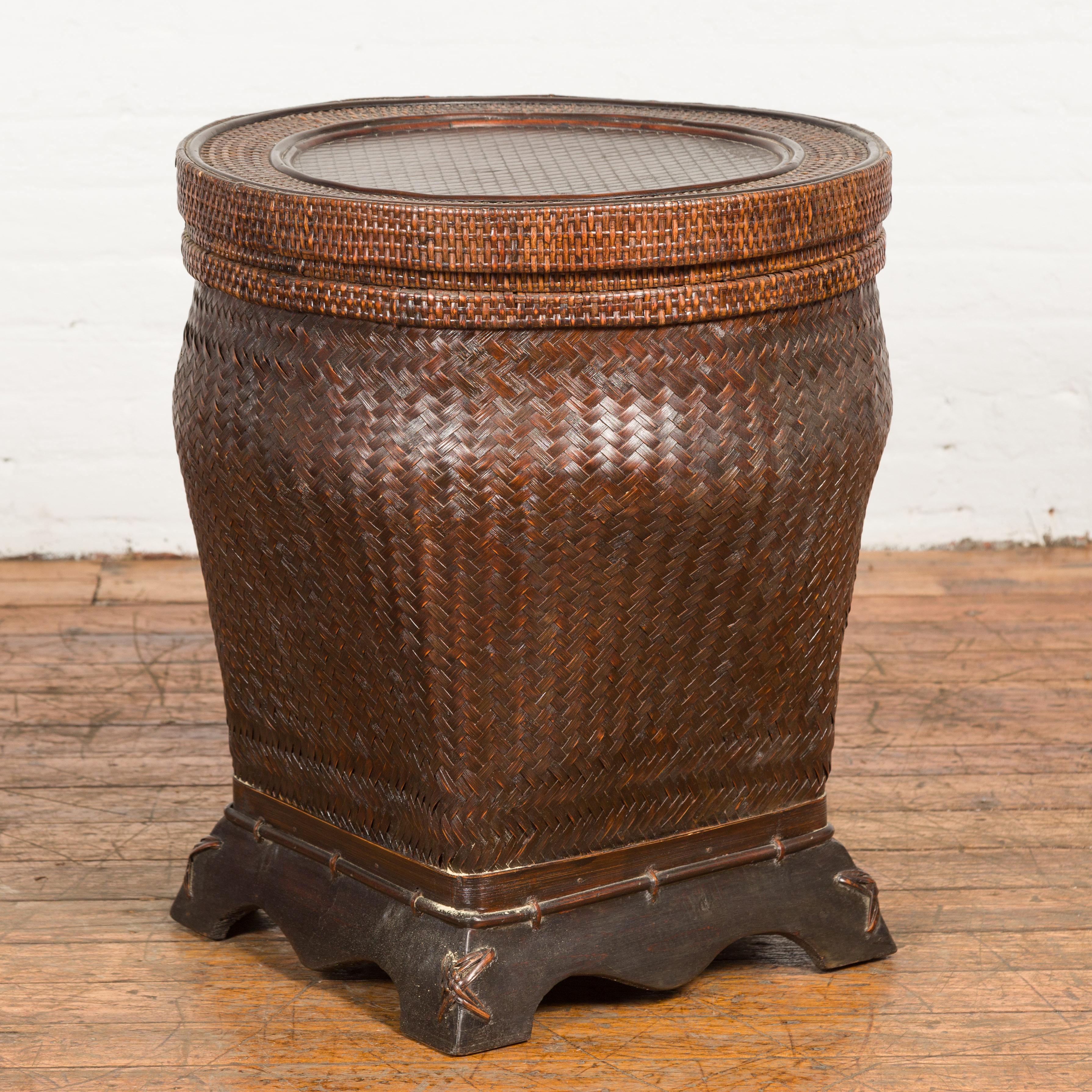 A tall rustic Thai vintage hand-woven rattan and bamboo storage basket from the mid 20th century, with hand-stitched cross motifs, circular lid, wooden scalloped base and dark brown patina. We have more baskets available in similar colors. Created