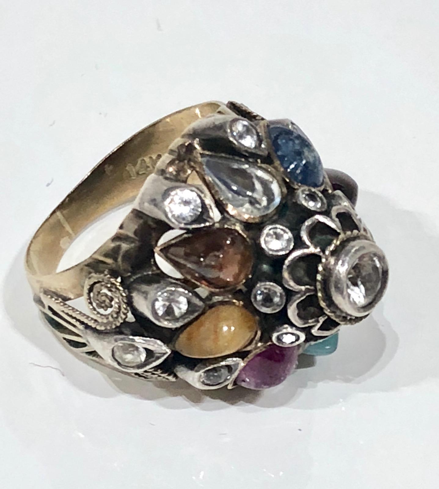 Dome style ring with set in 14 k gold and silver. Of opposing size and importance. Head dress inspired ring set with a variety of gems. 19 white sapphires plus blue sapphire, emerald, ruby, moonstone, and garnet, 8 in all.  Inner shank stamped with