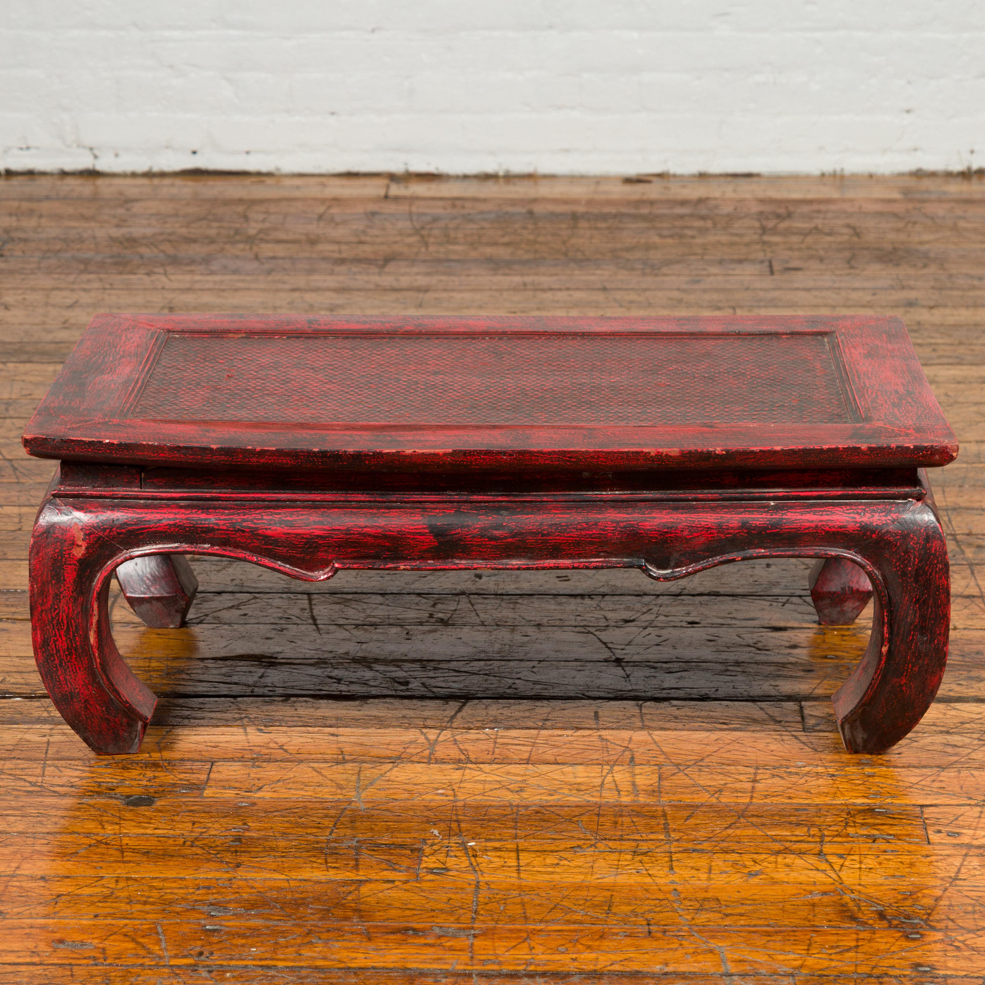 A vintage Thai coffee table from the mid-20th century with red lacquered finish, rattan inset and chow legs. Born in Thailand during the midcentury period, this coffee table features a rectangular top with central rattan inset, sitting above a