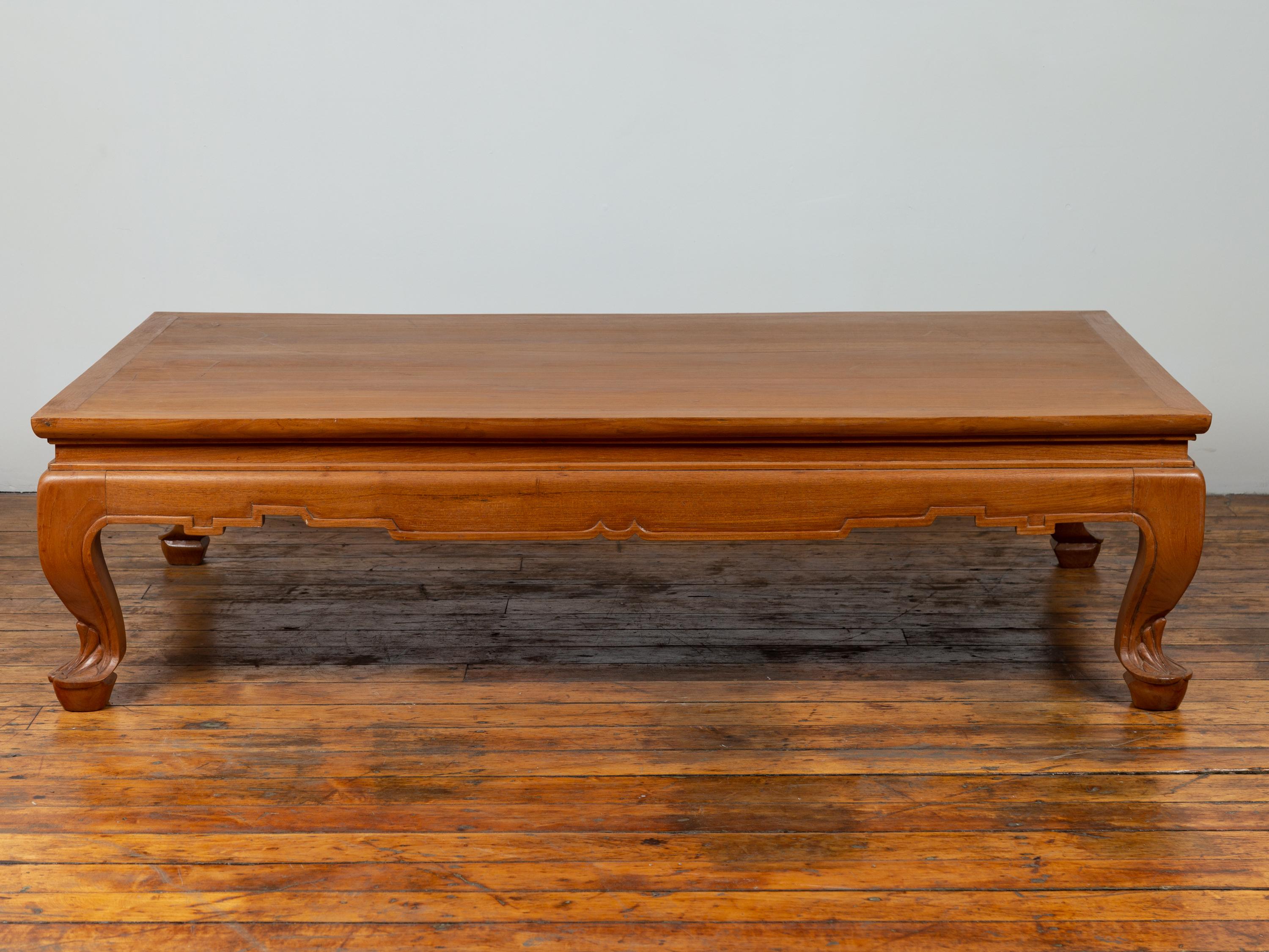 A vintage Thai teak coffee table from the mid-20th century, with waisted top, carved apron and cabriole legs. Born in Thailand during the mid-century period, this handsome coffee table features a rectangular planked waisted top sitting above a