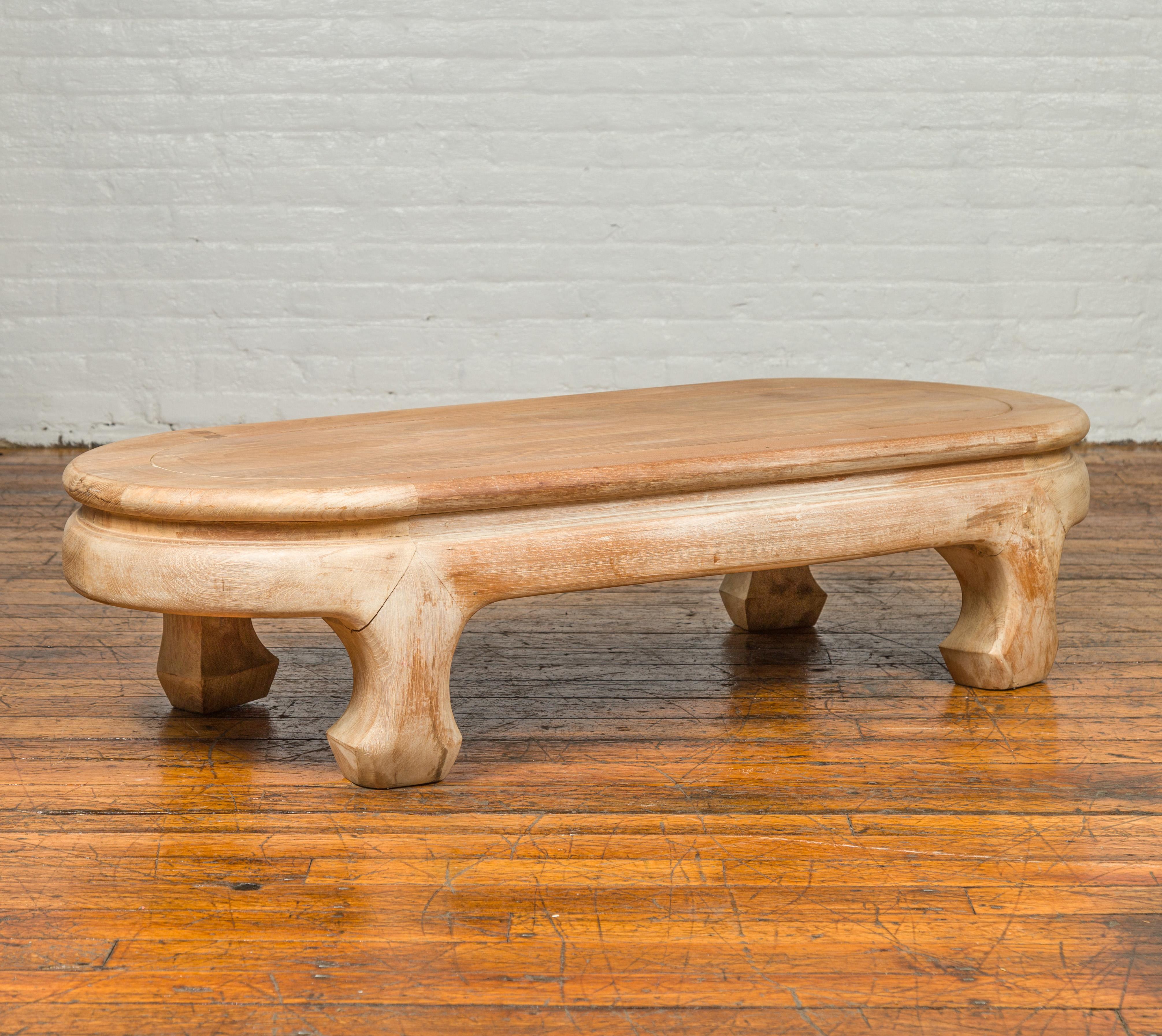A vintage Thai teak wood oval top coffee table from the mid-20th century, with whitewash finish and chow legs. Crafted in Thailand during the mid-century period, this teak wood coffee table features an oval waisted top, sitting above a base